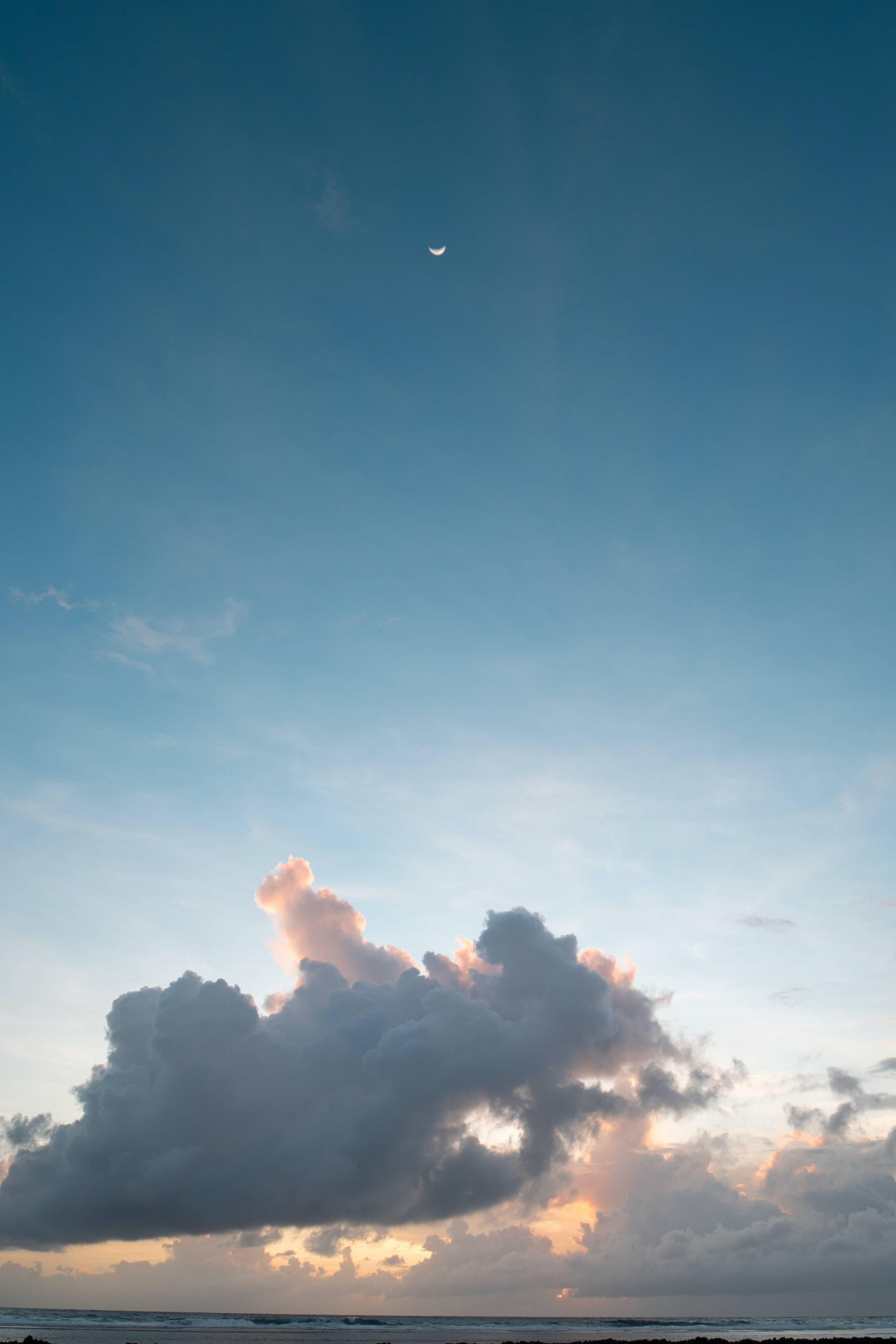Crescent 桌布 壁紙 — 海洋上空寧靜的日落，新月和柔和的粉紅雲朵映襯著漸變的藍色天空。