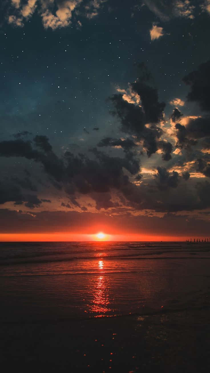 海灘 桌布 壁紙 — 海洋上空熾熱的日落，星星在戲劇性的多雲天空中出現。