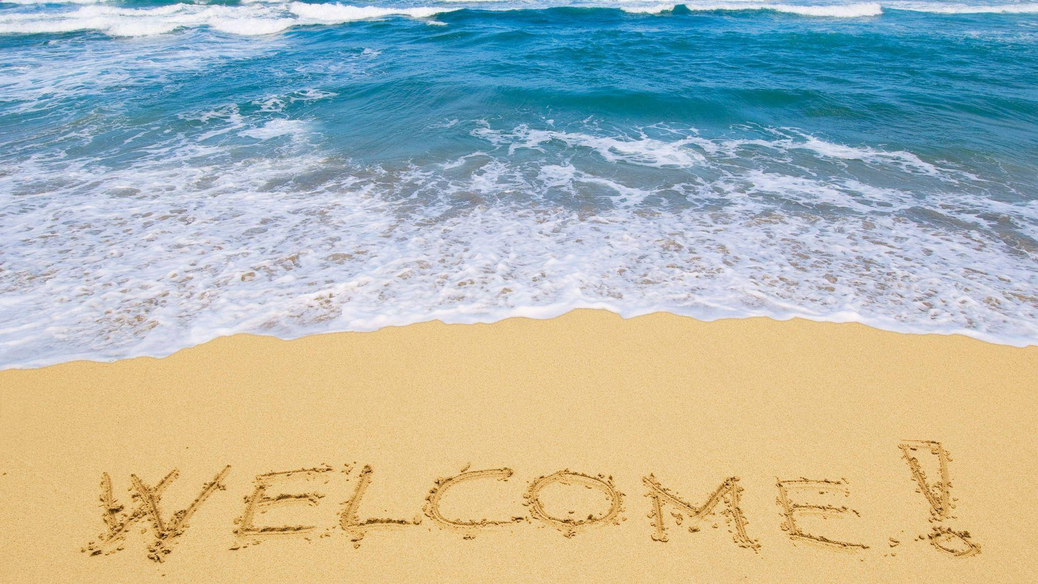Welcome 桌布 壁紙 — 海浪輕輕拍打金色沙灘，沙灘上以粗體、陽光燦爛的字體寫著「WELCOME!」。