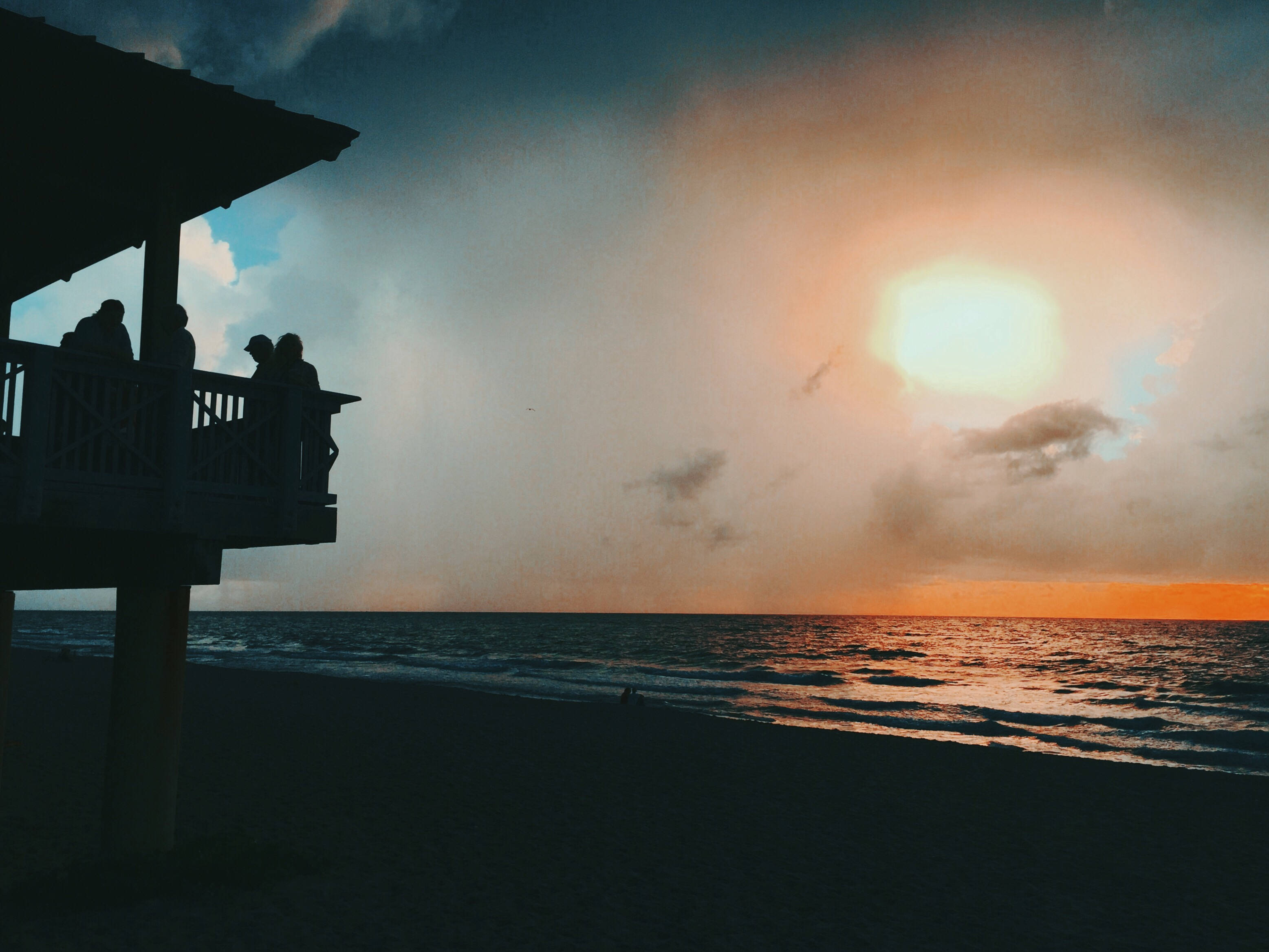 Silhouette 桌布 壁紙 — 海灘碼頭上的剪影人物凝視著海洋上壯麗的日落，伴隨著火紅色的雲彩。
