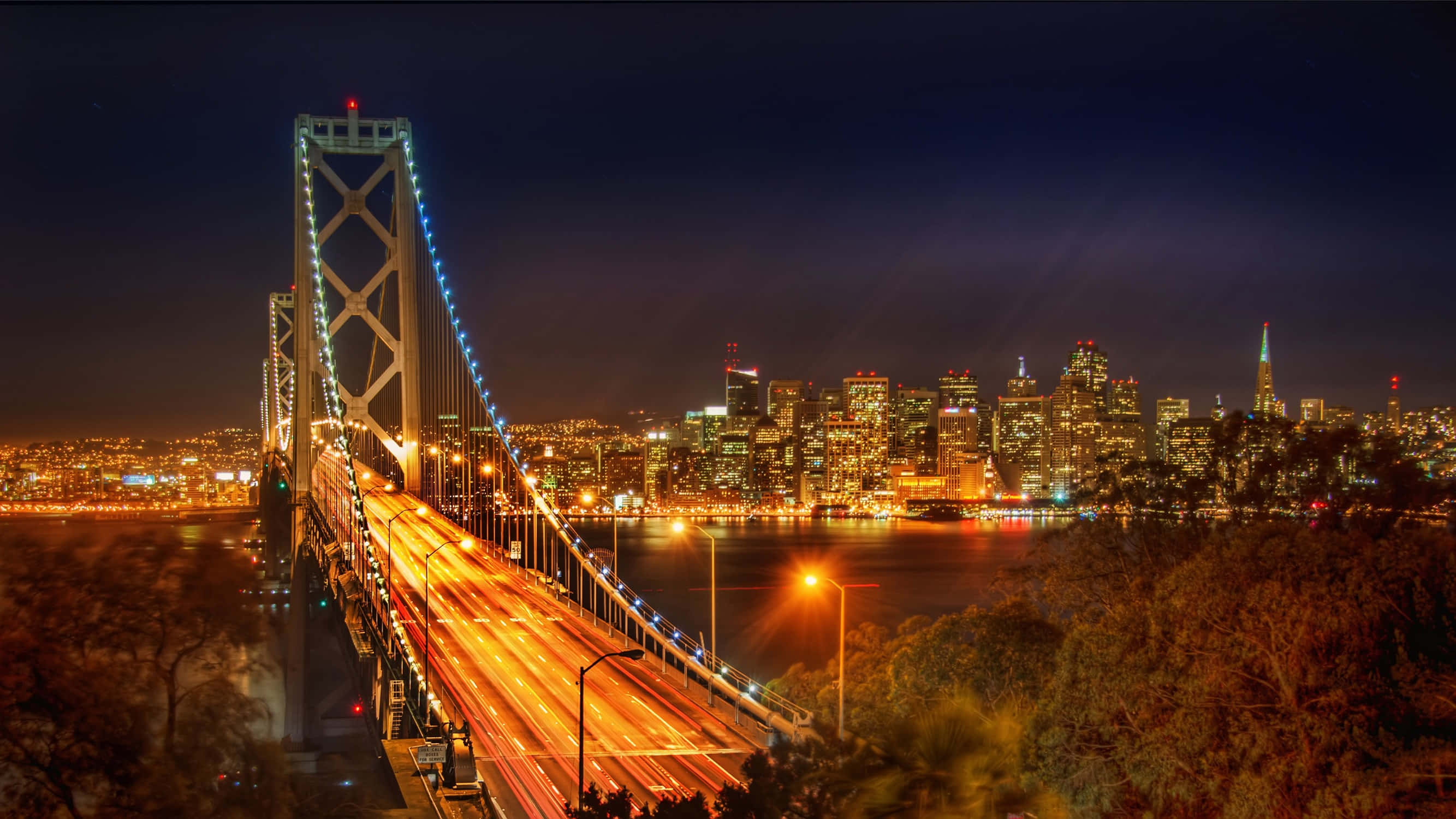 桌布 壁紙 — 海灣大橋的迷人夜景，城市燈光在水面上閃爍，車流形成光軌。