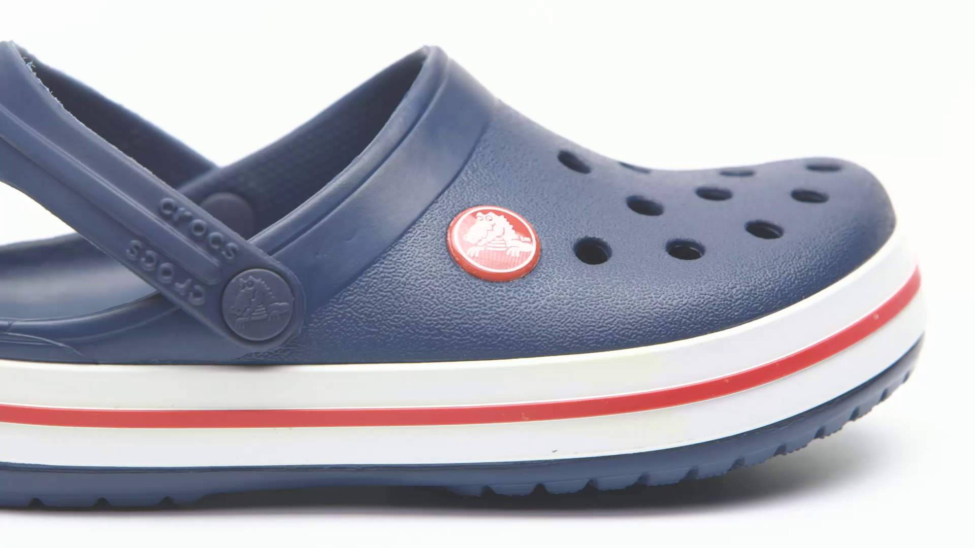 Crocs 桌布 壁紙 — 海軍藍色 Crocs 木屐的特寫，鞋底有紅白條紋，背景為白色。
