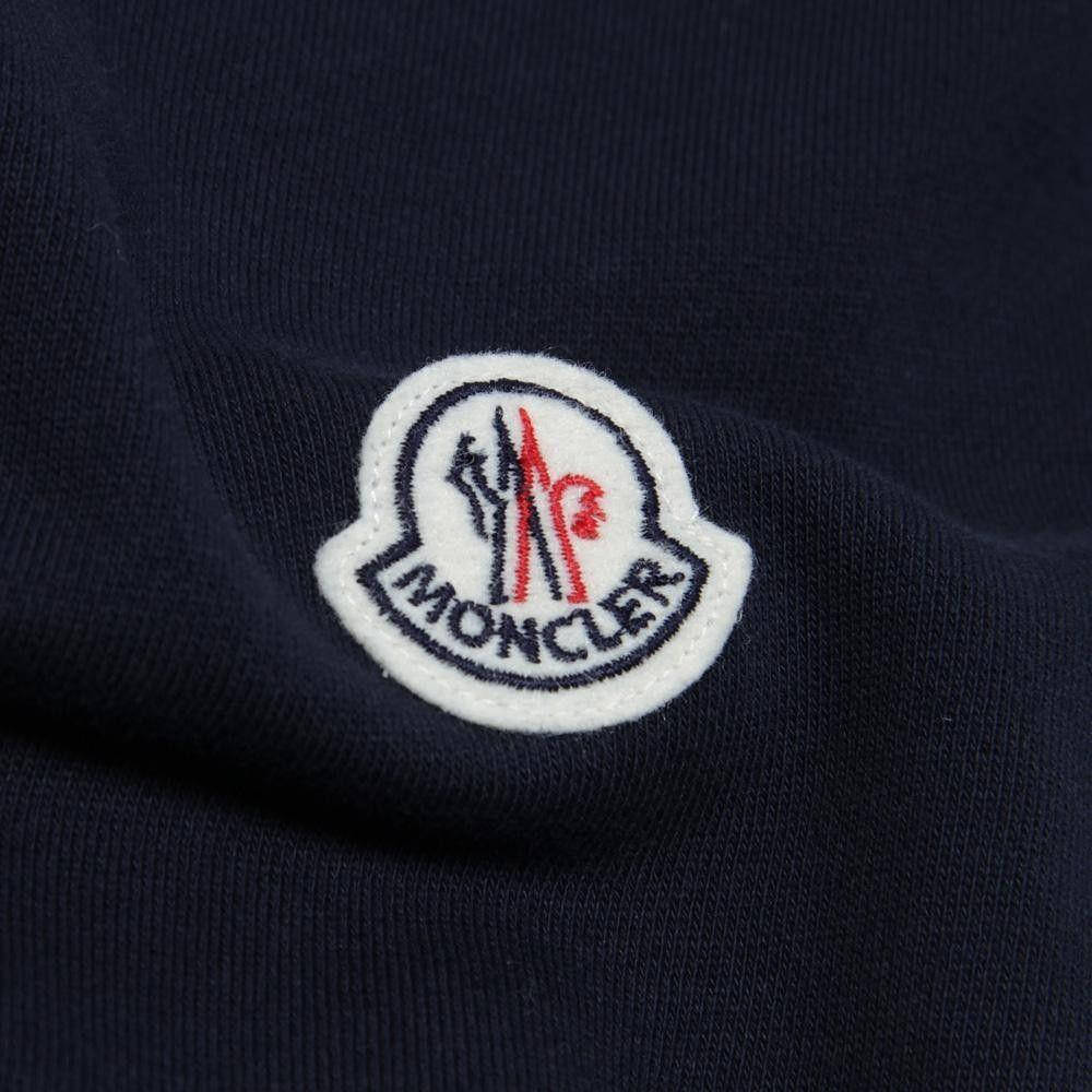 Moncler 桌布 壁紙 — 海軍藍色Moncler品牌布章特寫，布章上有紅色和黑色標誌，位於有紋理的布料上。