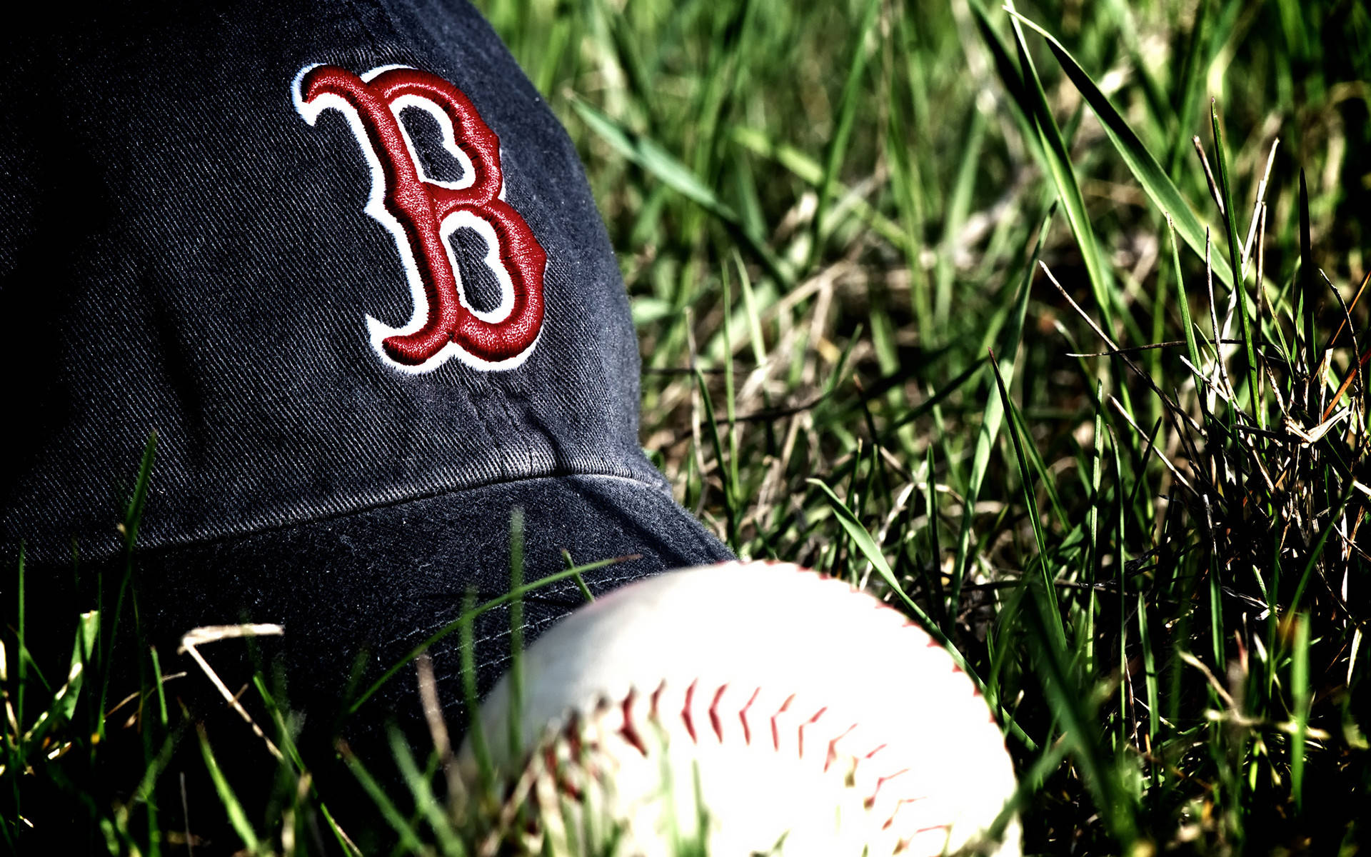 Red Sox 桌布 壁紙 — 海軍藍色棒球帽，帶有紅色刺繡的「B」和白色棒球，放在陽光照耀的綠色草地上。