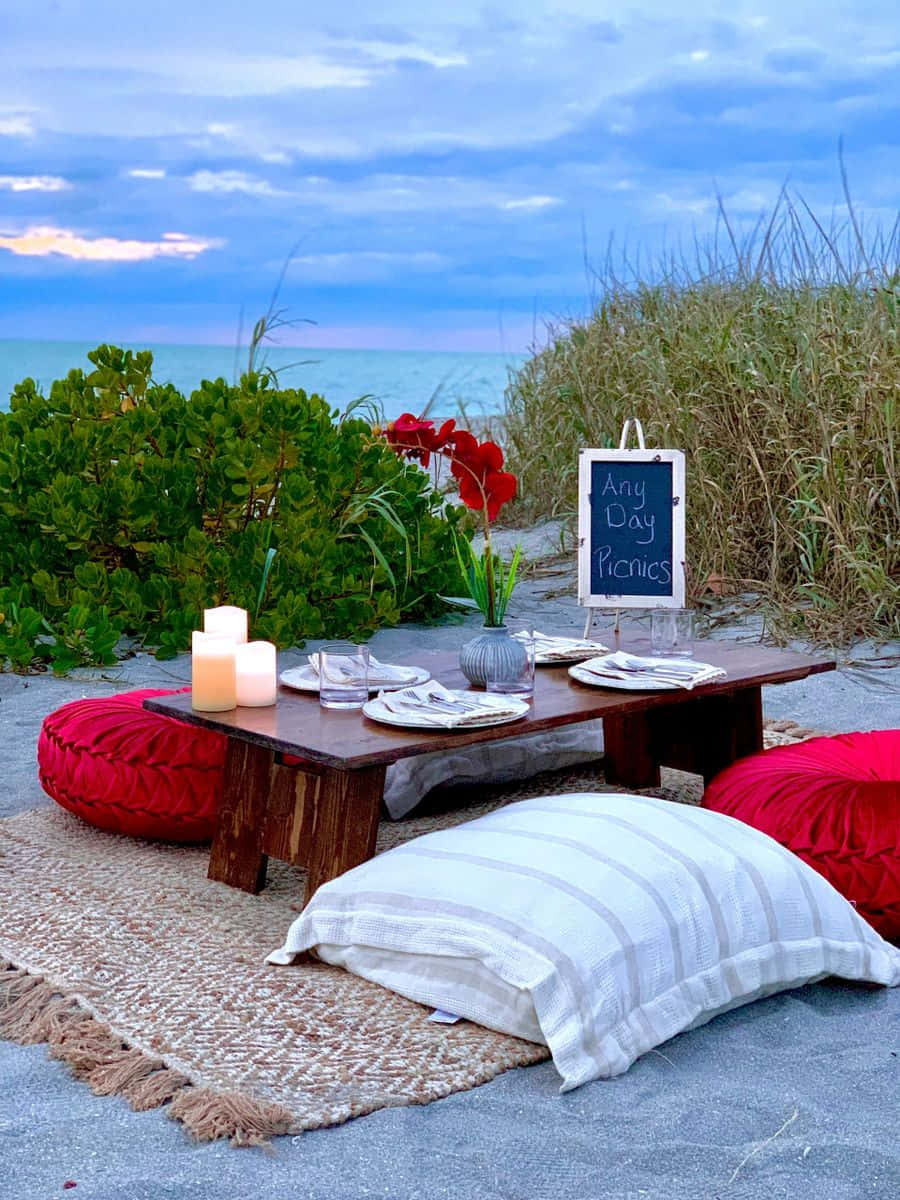 Beach Picnic 桌布 壁紙 — 海邊野餐佈置，木桌上放有紅色坐墊和蠟燭，背景是暮色天空。