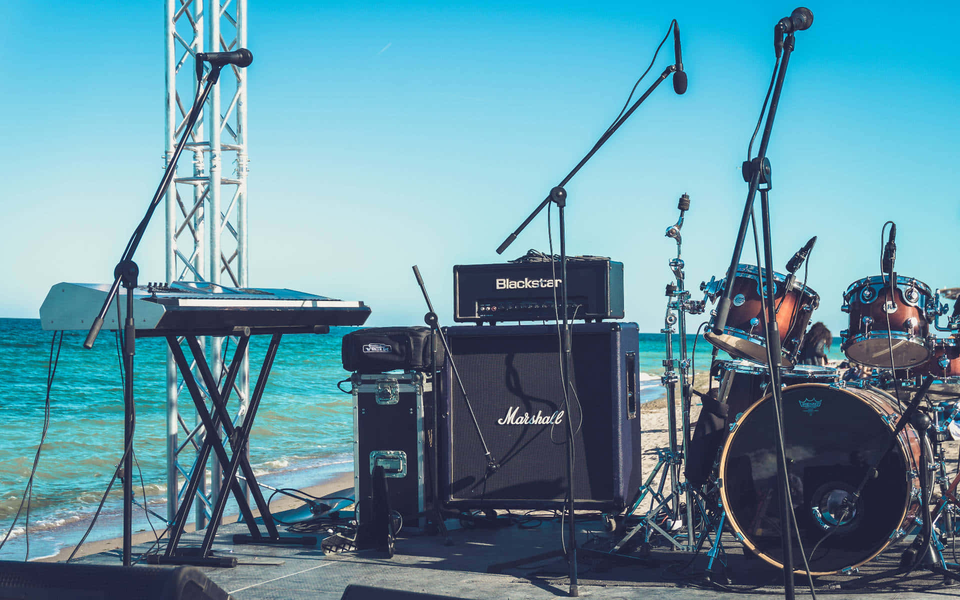 Marshall 桌布 壁紙 — 海邊音樂舞台，配有鼓組、鍵盤和 Marshall 擴音器，背景是碧綠海洋和晴朗藍天。