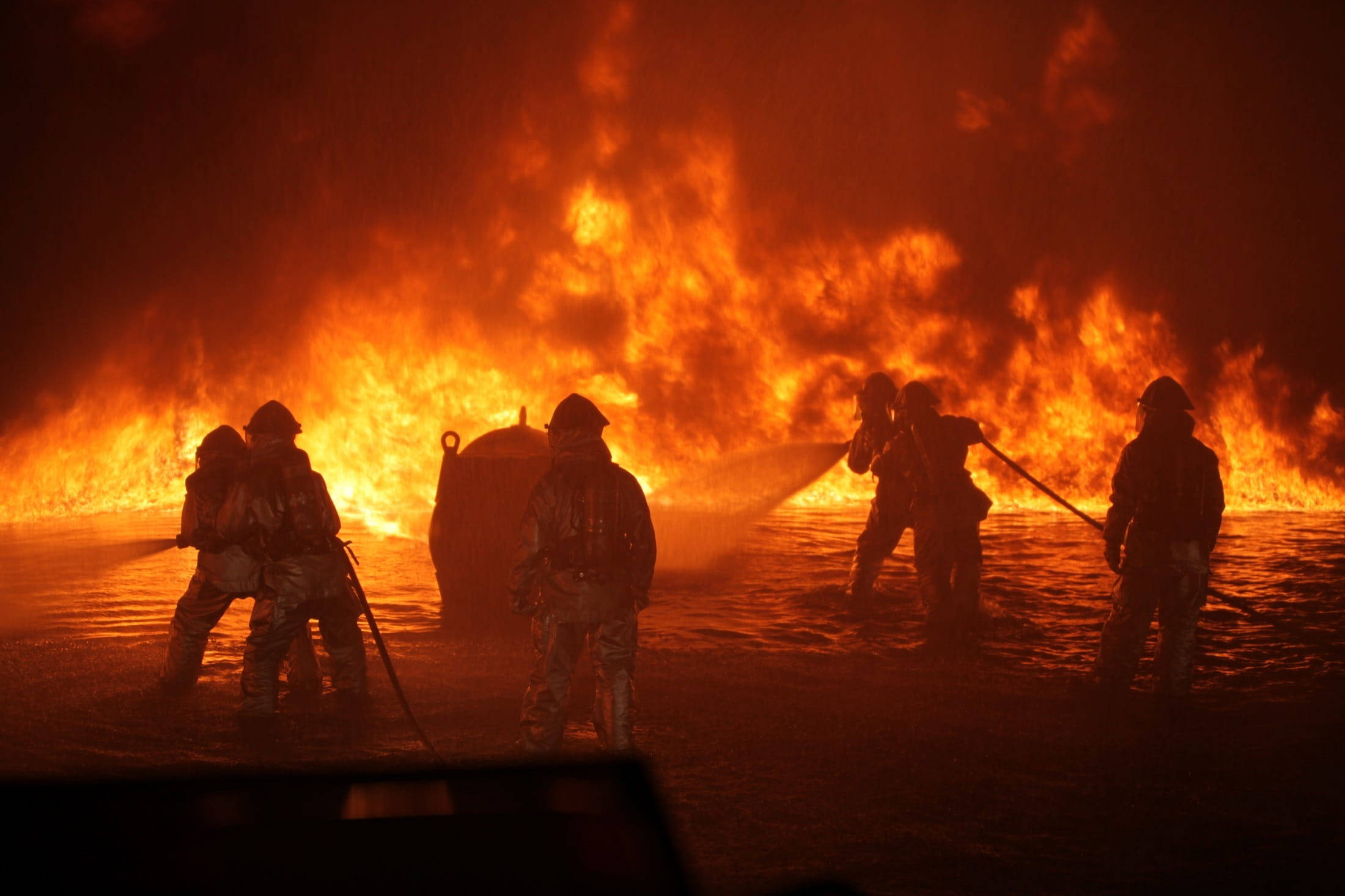Firefighter 桌布 壁紙 — 消防員在剪影中於夜間用軟管在強烈的橙色火焰下撲滅大規模山火。