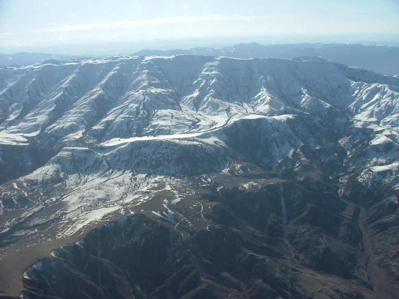 Tajikistan 桌布 壁紙 — 淡藍色天空下，白雪覆蓋的山脈，崎嶇的山峰和蜿蜒的山谷的鳥瞰圖。