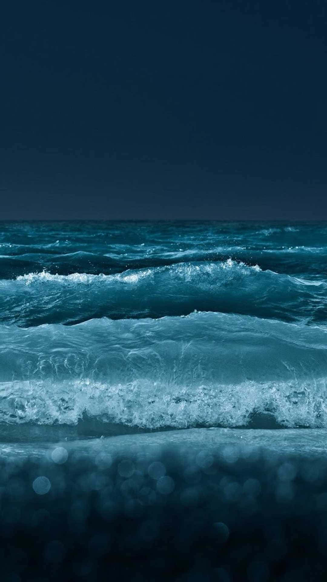 Beach Phone 桌布 壁紙 — 深沉的藍綠色海浪在深邃的夜空下拍打著模糊的海岸線。