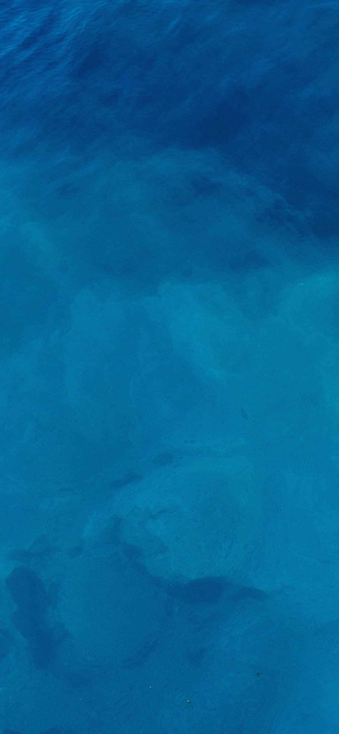 Plain Blue 桌布 壁紙 — 深海藍色海水的航拍視圖，揭示水面下的沙質海床圖案。