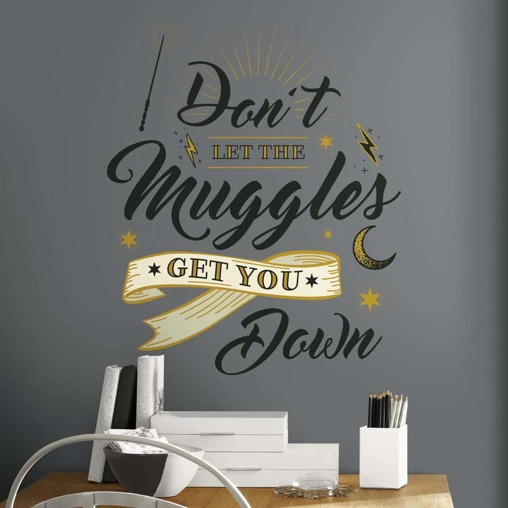 Harry Potter Muggle 桌布 壁紙 — 深灰色牆上有一個時尚的哈利波特語錄貼紙，帶有金色點綴和魔法符號，位於一個有白色儲物盒和美術用品的木桌上。