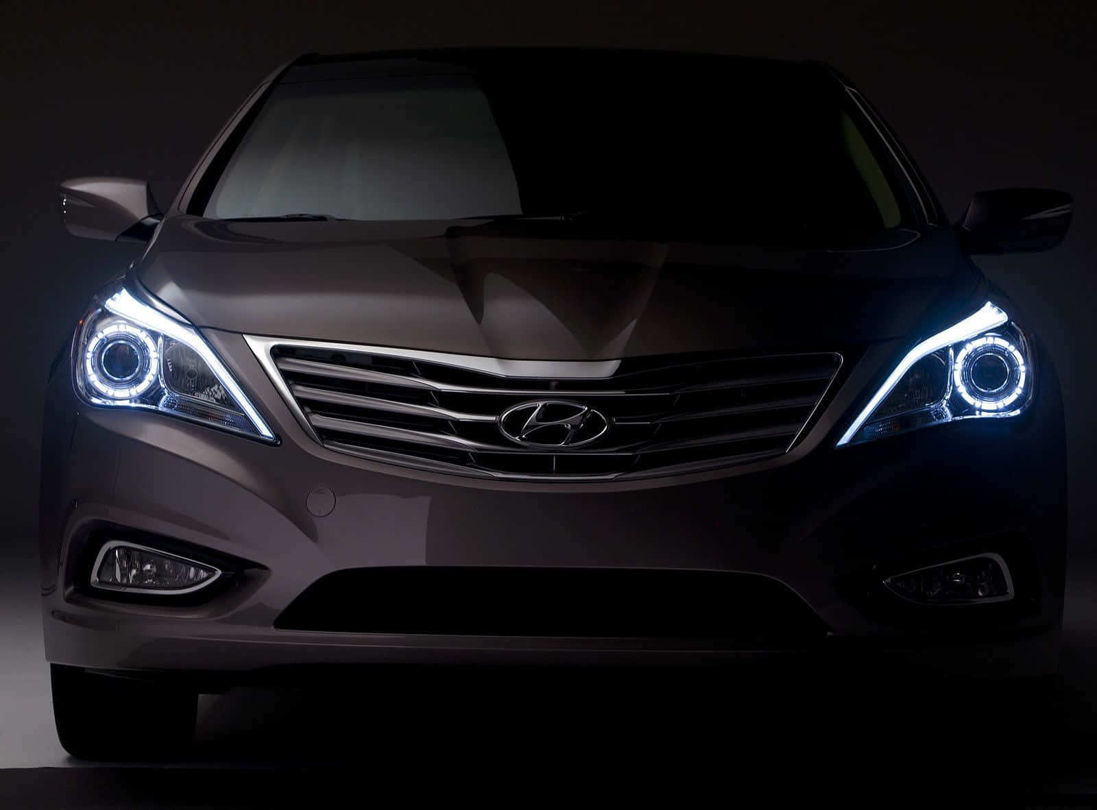 Hyundai Azera 桌布 壁紙 — 深灰色現代轎車的正面視圖，帶有發光的藍色光環頭燈，背景為黑色攝影棚。