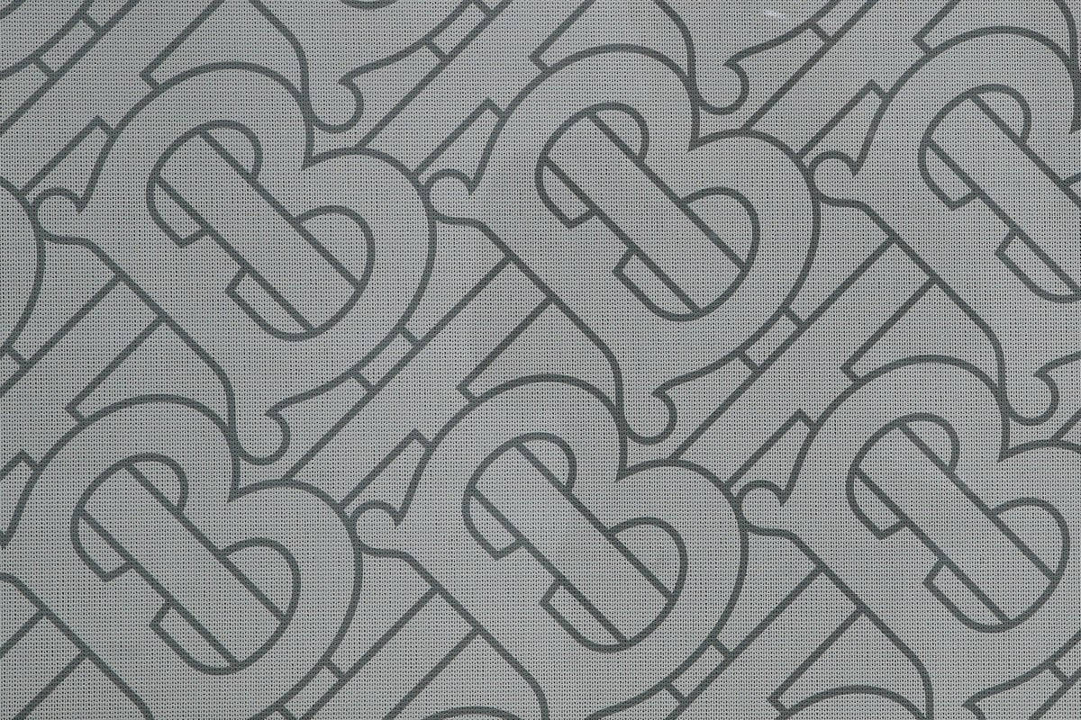 Designer Logo 桌布 壁紙 — 深灰色風格化B字母的重複字母組合圖案，位於有紋理的淺灰色布料背景上。