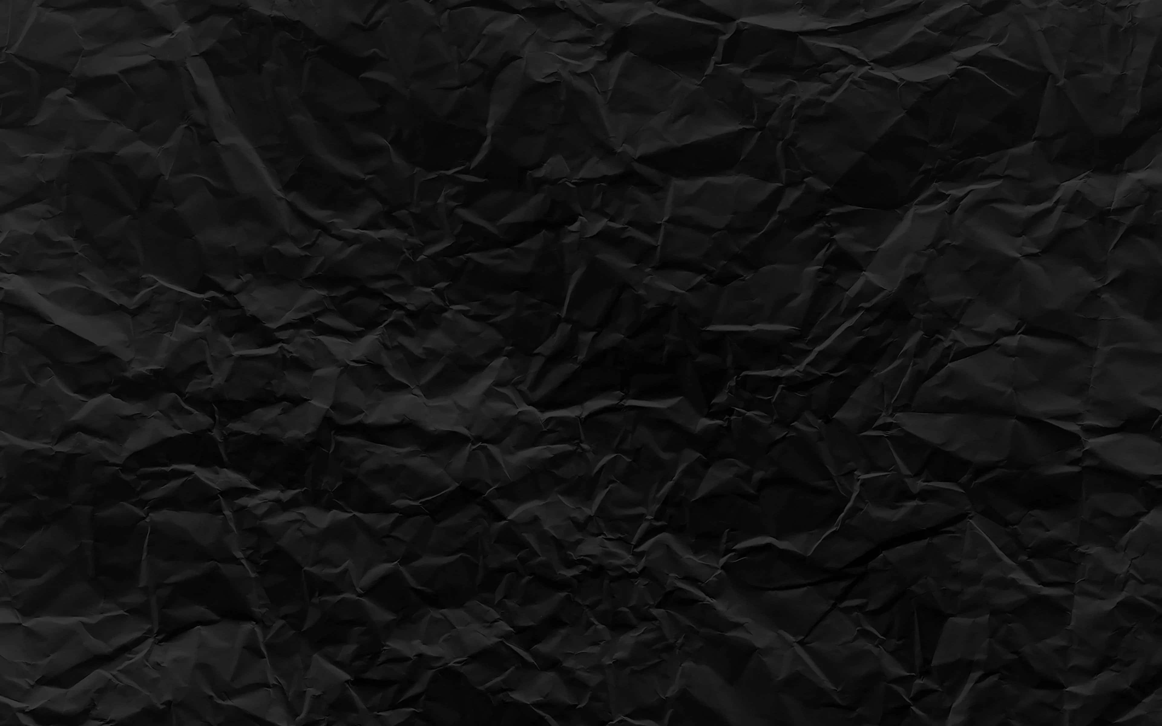 Black Paper Texture 桌布 壁紙 — 深皺黑色紙張的特寫，帶有紋理摺痕和細微陰影，營造出陰鬱的抽象表面。