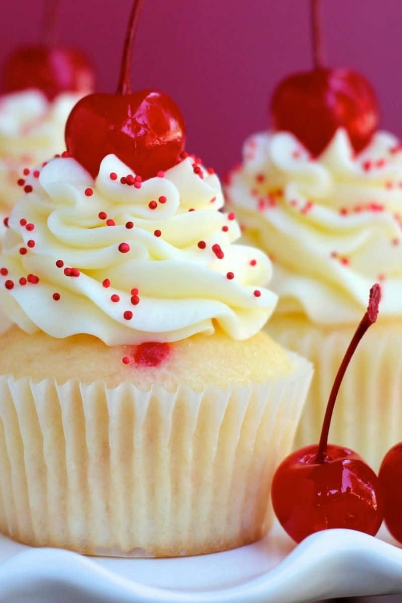 Cupcake 桌布 壁紙 — 深粉紅色背景上，奶油香草紙杯蛋糕的近距離特寫，上面有光澤的櫻桃和紅色糖粒。