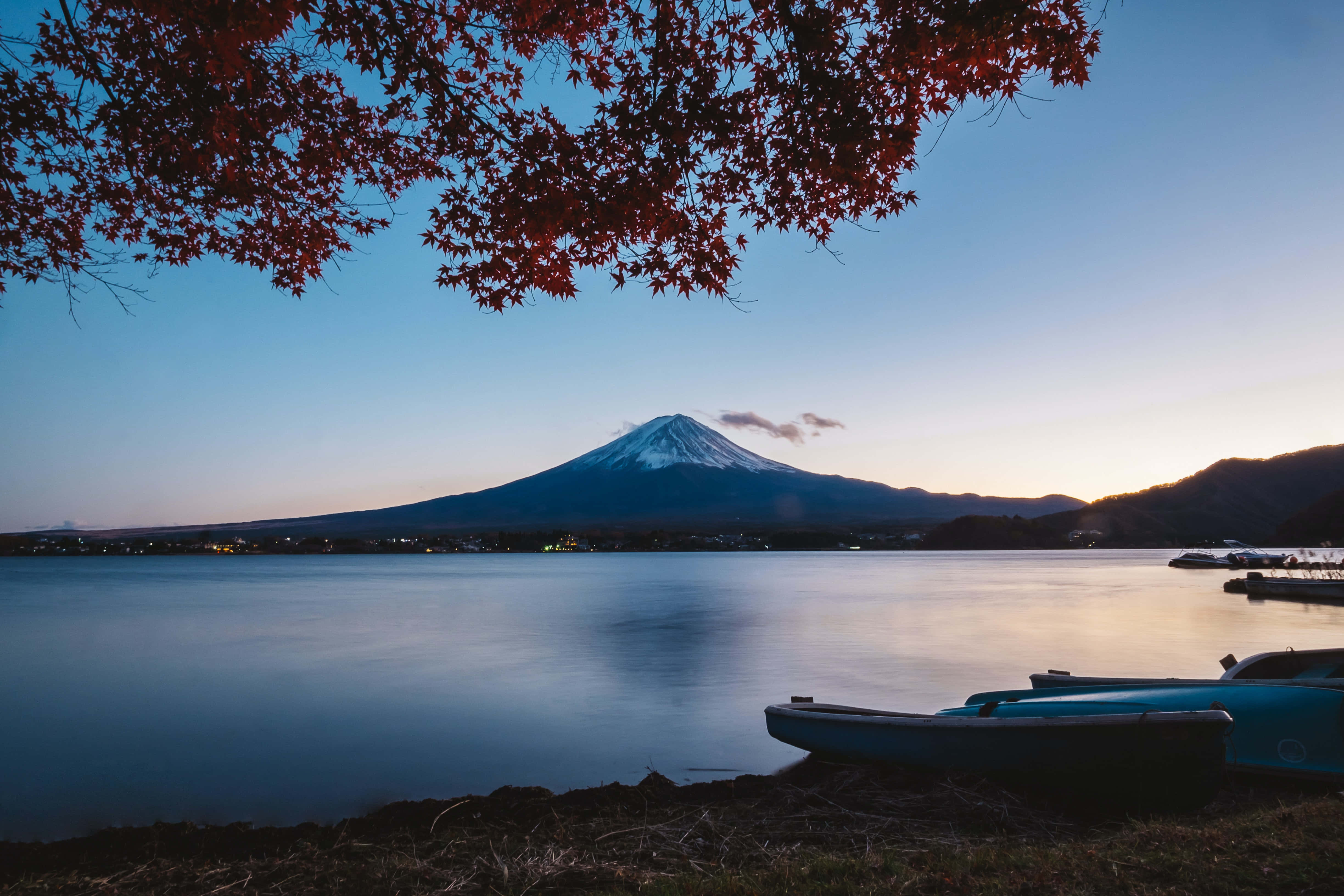 日本 桌布 壁紙 — 深紅的楓葉框住寧靜的暮色景色，積雪的富士山倒映在平靜的水面上，附近停泊著船隻。