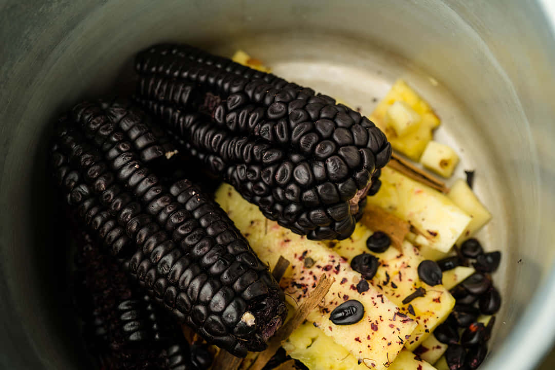 Purple Corn 桌布 壁紙 — 深紫色玉米芯藏於不鏽鋼鍋中的鳳梨塊和香料之間。