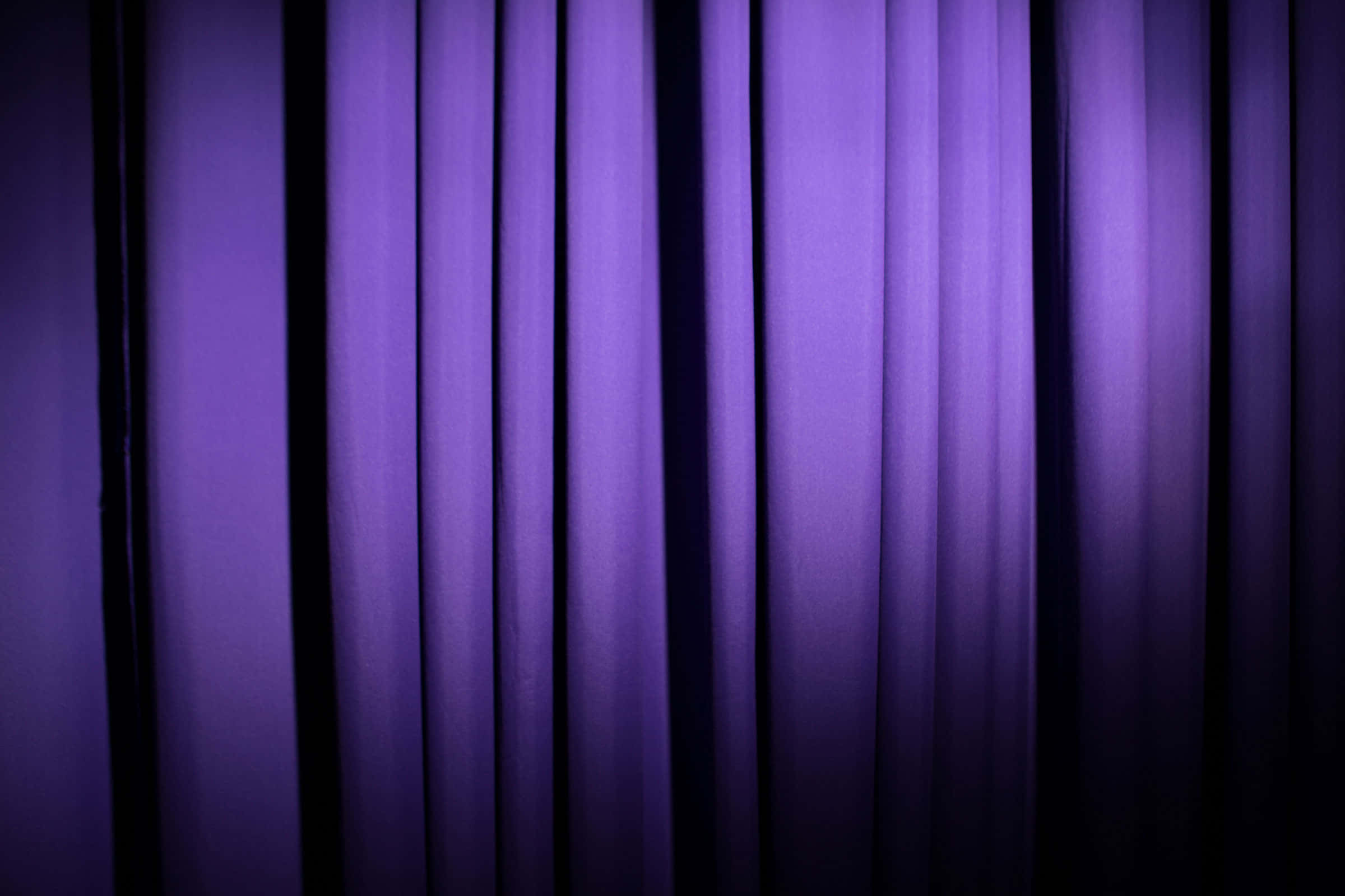 Purple Curtains 桌布 壁紙 — 深紫色的劇院窗簾以柔軟的垂直褶皺懸掛，由背後的戲劇性舞台燈光照亮。