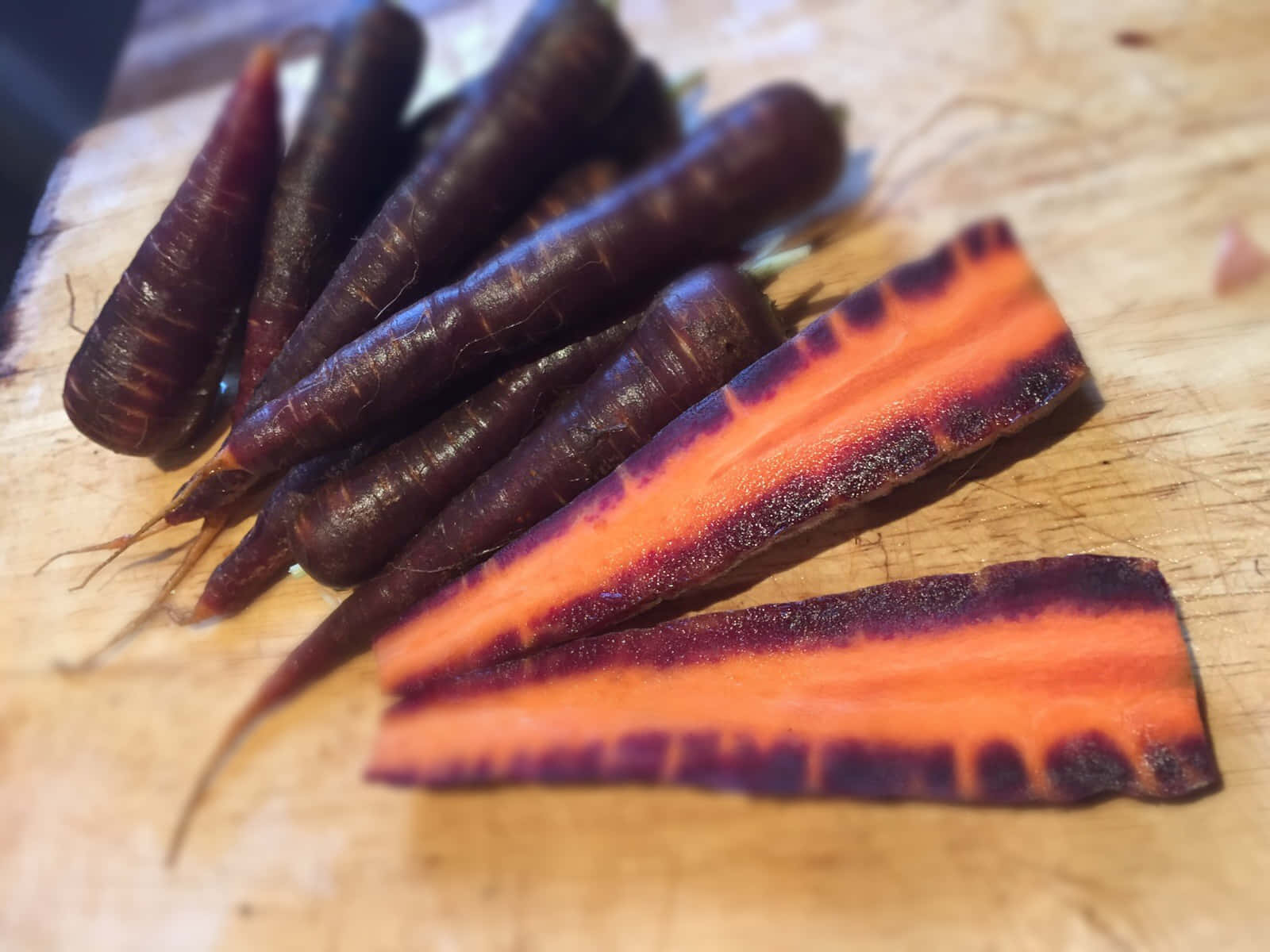 Purple Carrots 桌布 壁紙 — 深紫色胡蘿蔔帶有鮮豔的橙色內部，放置在質樸的木製砧板上。