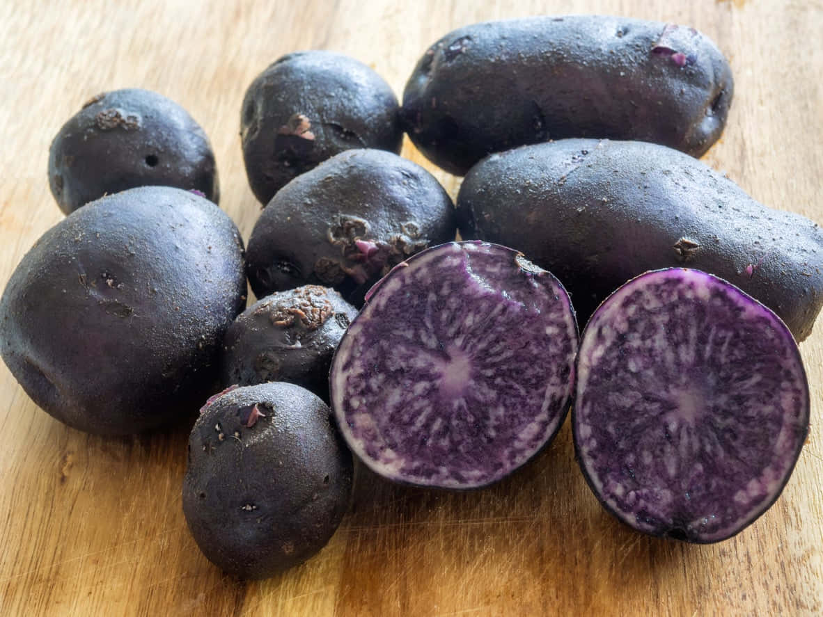 Purple Potato 桌布 壁紙 — 深紫色馬鈴薯帶有鮮豔的內部果肉，放在溫暖的木製砧板上。
