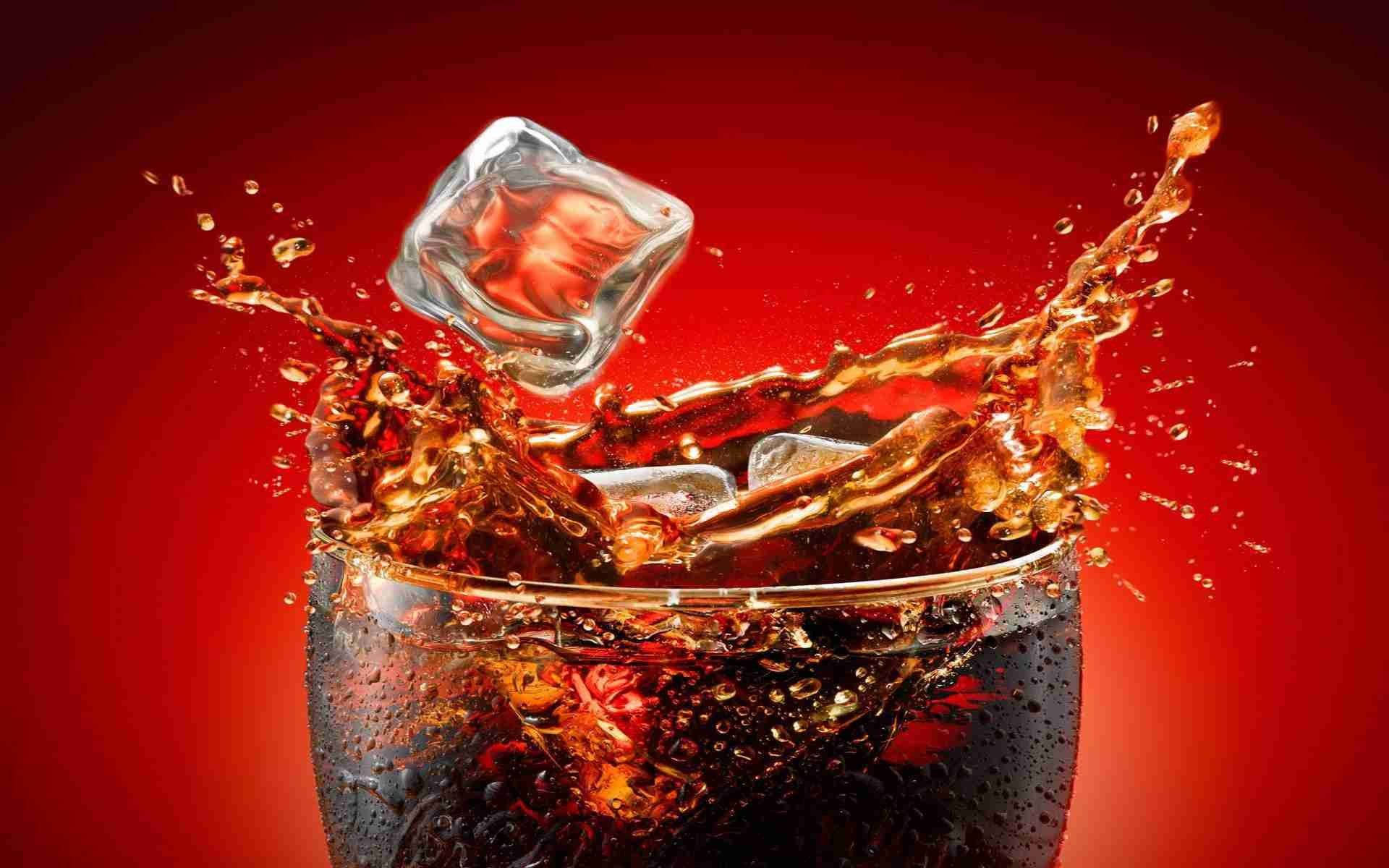 Drink 桌布 壁紙 — 深色可樂從玻璃杯中噴出，冰塊撞擊在鮮紅色的背景上，形成動態的飛濺。