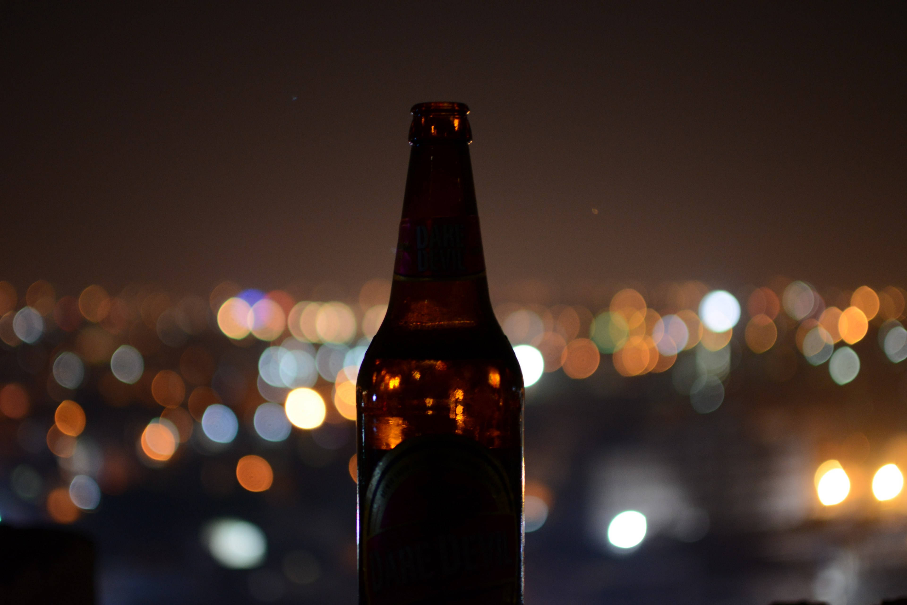 Beer 桌布 壁紙 — 深色啤酒瓶剪影，襯托著夜間充滿活力的散景城市景觀。