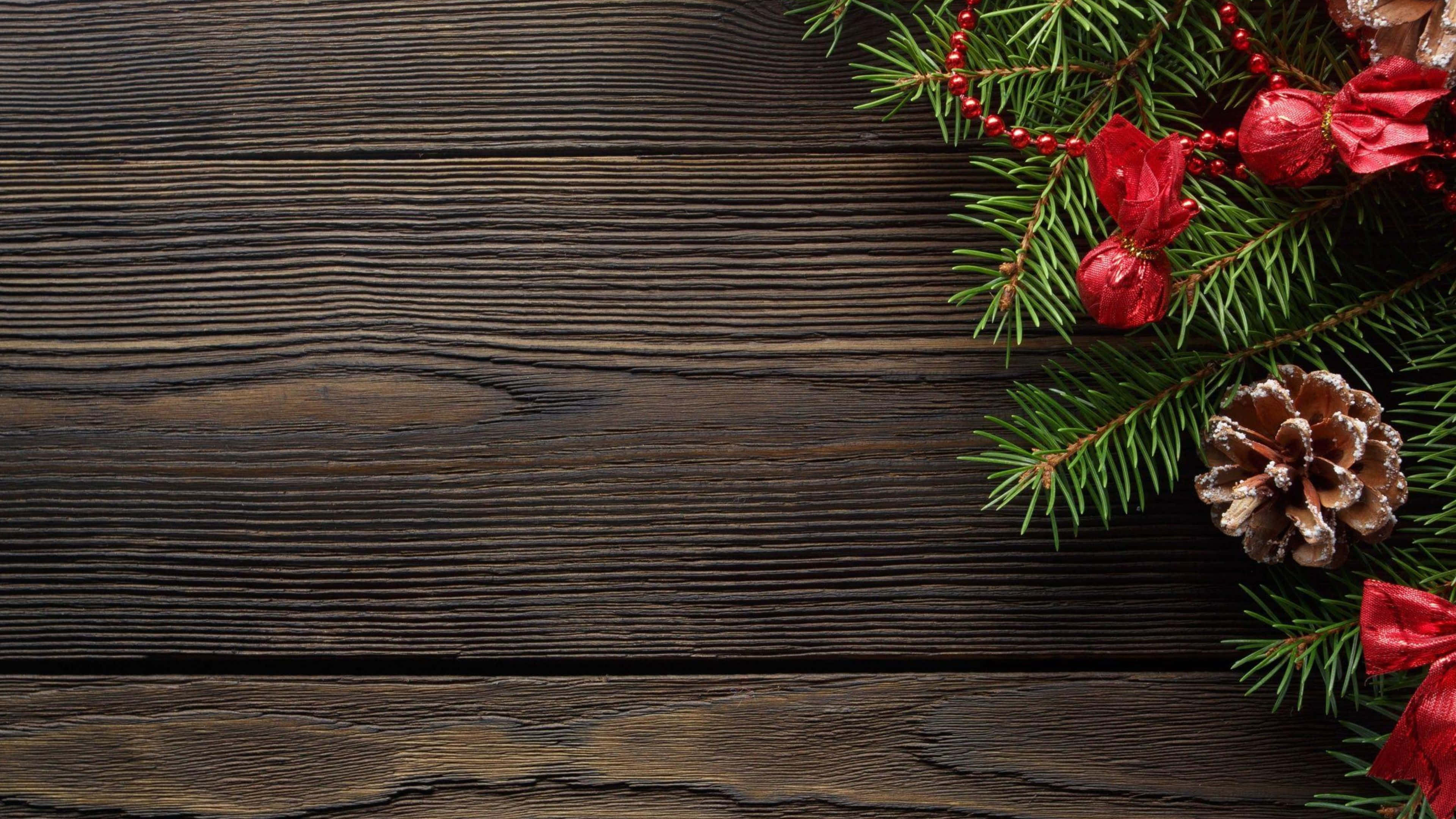 Rustic Christmas 桌布 壁紙 — 深色木板上，右上角裝飾著節日綠色松枝、紅色漿果和松果。