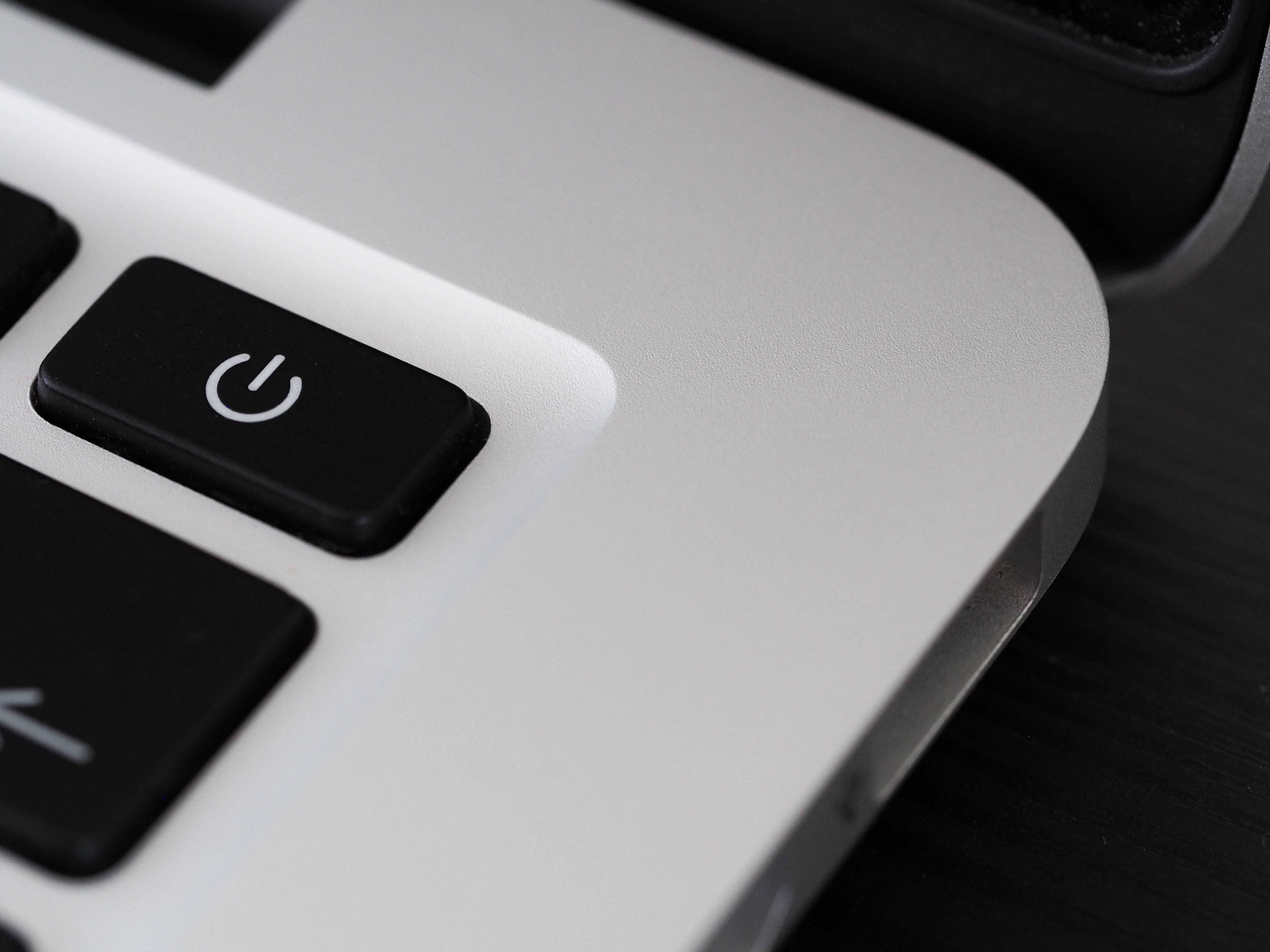 aesthetic tumblr laptop 桌布 壁紙 — 深色木質表面上，時尚銀色筆記型電腦的電源按鈕特寫，帶有黑色按鍵。