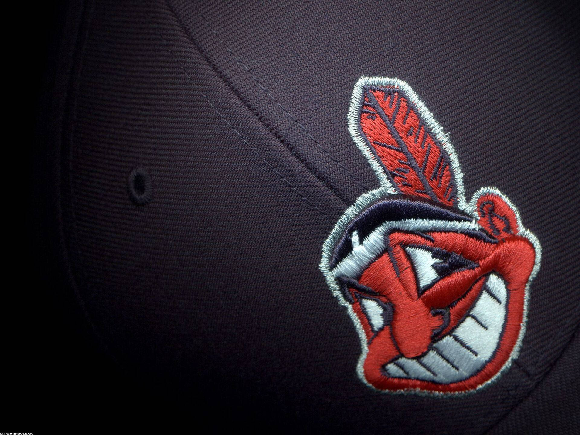 Cleveland Indians 桌布 壁紙 — 深色棒球帽上紅色、白色和灰色刺繡的Chief Wahoo標誌特寫，可見縫線和布料質感。