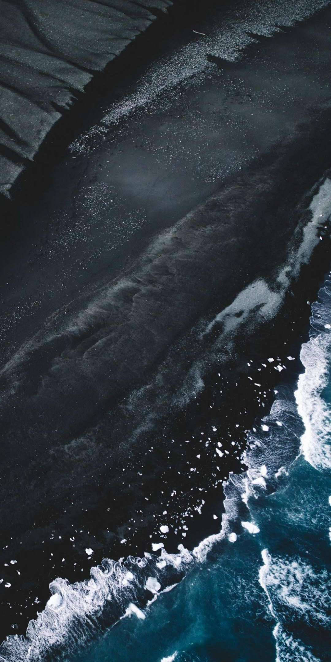 海灘 iPhone 桌布 壁紙 — 深色火山沙灘與帶有白色泡沫的碧綠海浪相遇的鳥瞰圖。