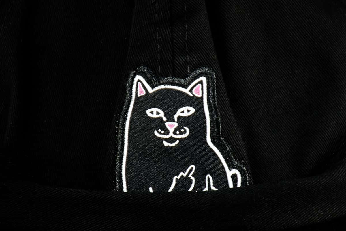 ripndip 桌布 壁紙 — 深色牛仔布上黑色刺繡貓咪貼章的近距離特寫，貓咪豎起中指，內耳和鼻子為粉紅色。