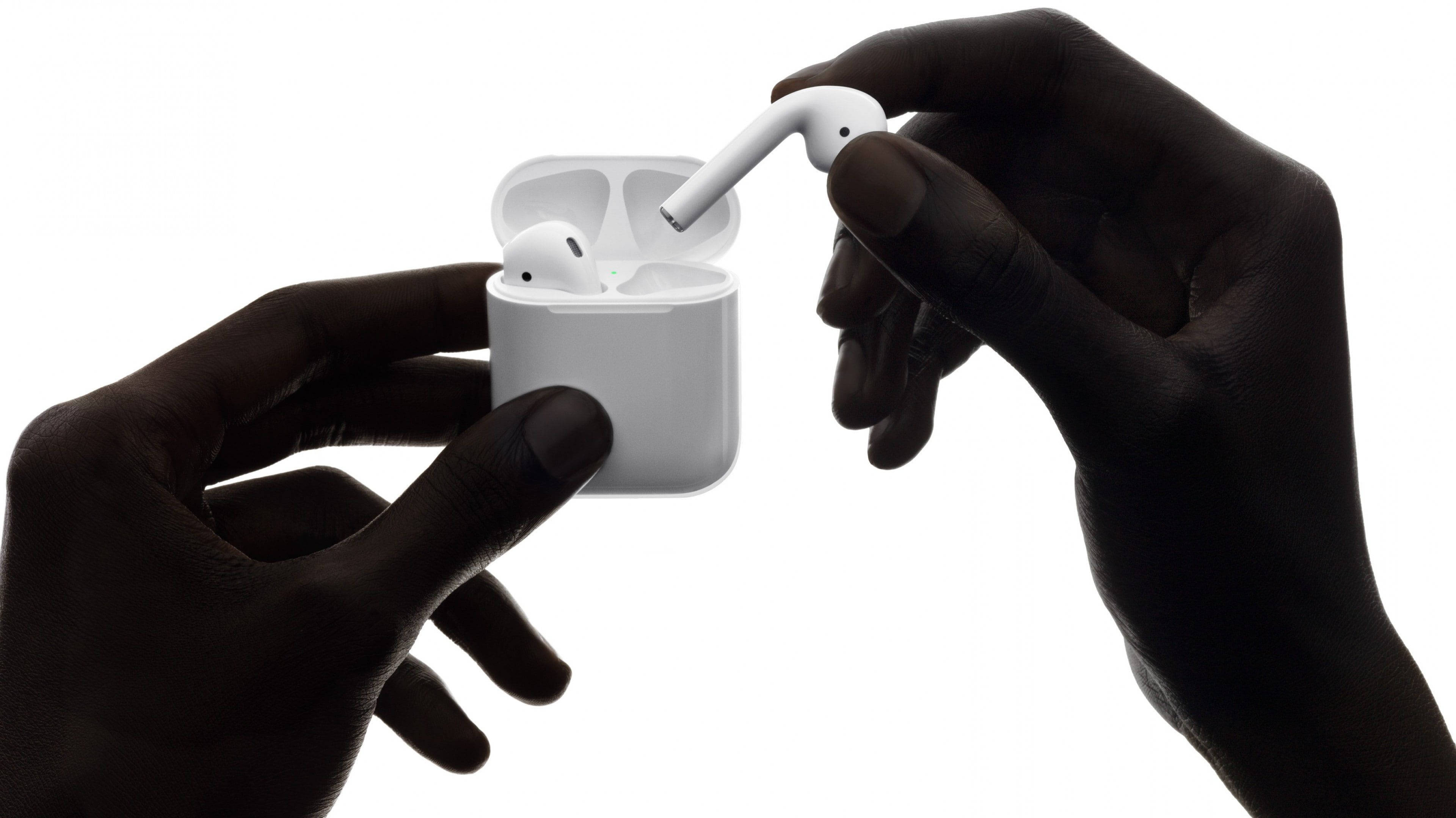 Airpods 桌布 壁紙 — 深色皮膚的手在純白色背景上，輕輕地從時尚的充電盒中取出一個白色無線耳機。