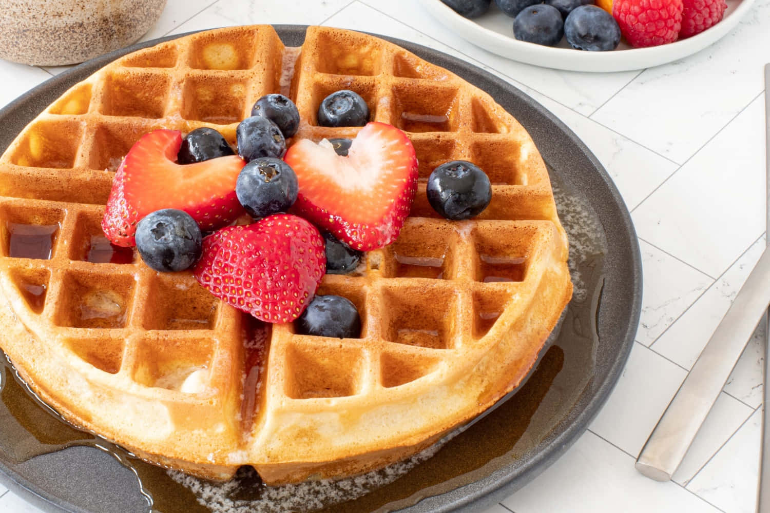 Waffle 桌布 壁紙 — 深色盤子上放有金黃色鬆餅，配上新鮮草莓、藍莓和糖漿。