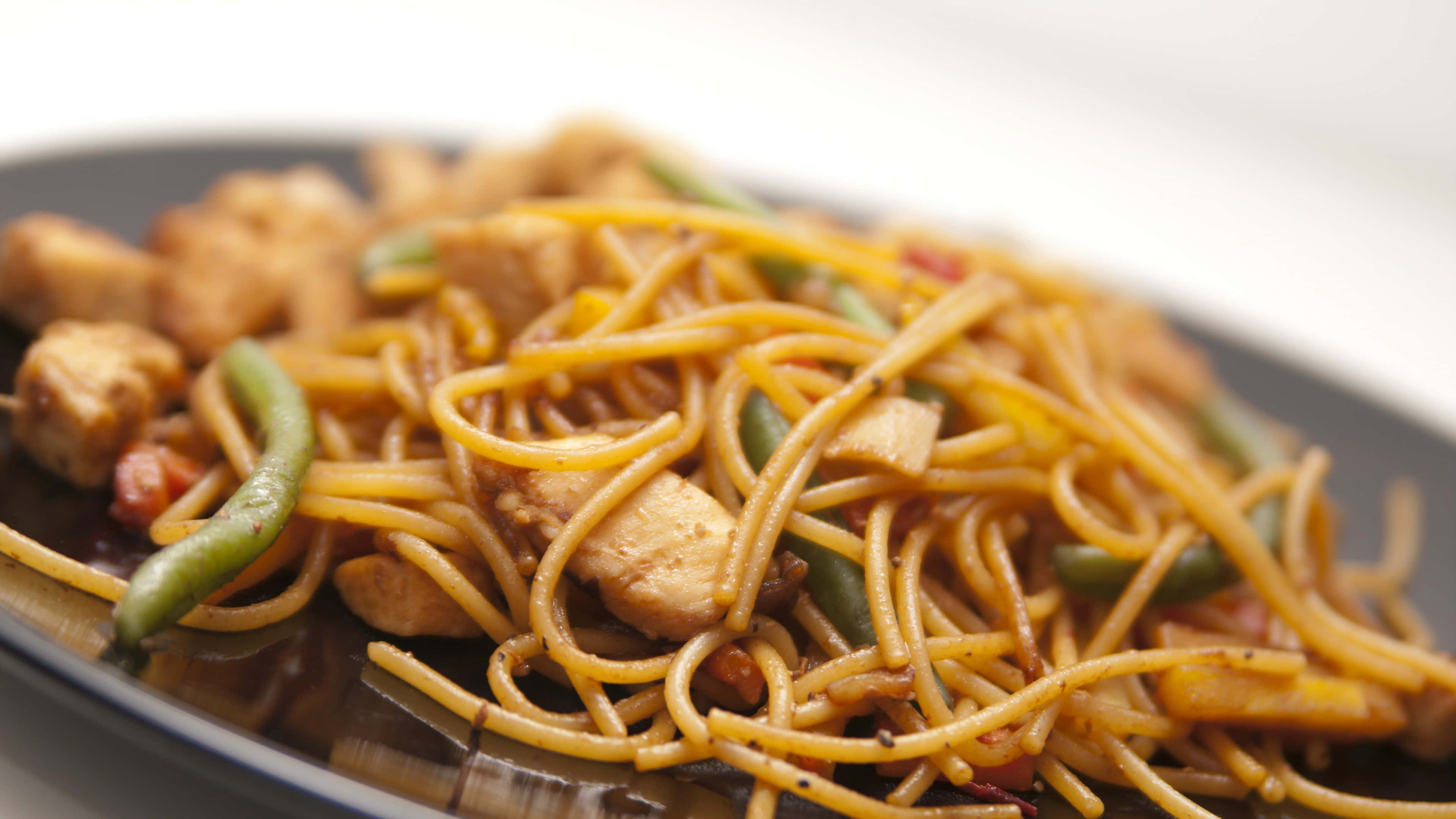 4K Pasta 桌布 壁紙 — 深色盤子上的雞肉青豆炒麵特寫。