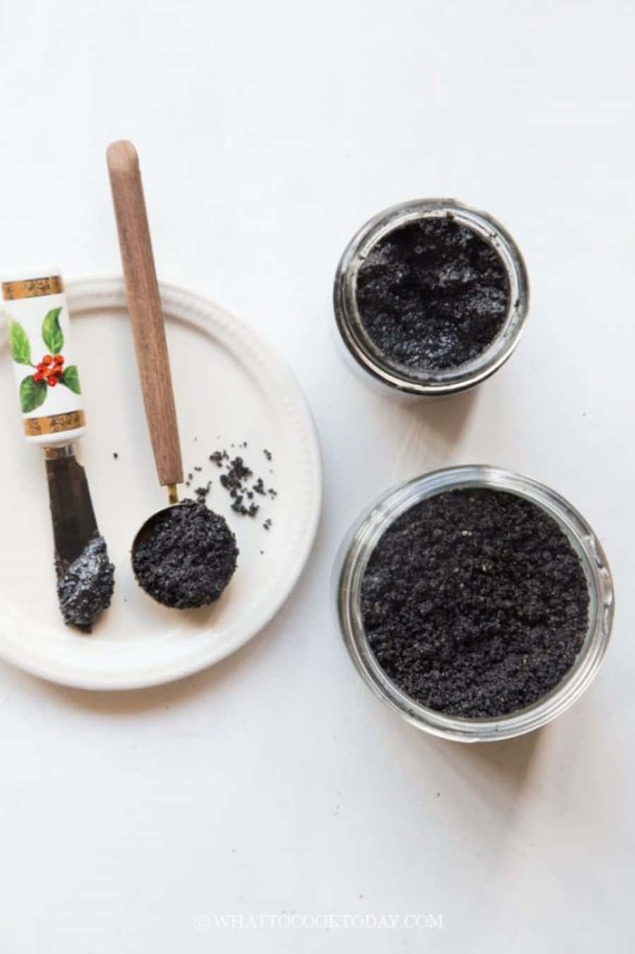 Black Sesame 桌布 壁紙 — 深色粗黑糖磨砂膏裝在玻璃罐中，配木勺放在白色盤子上，俯拍鏡頭。