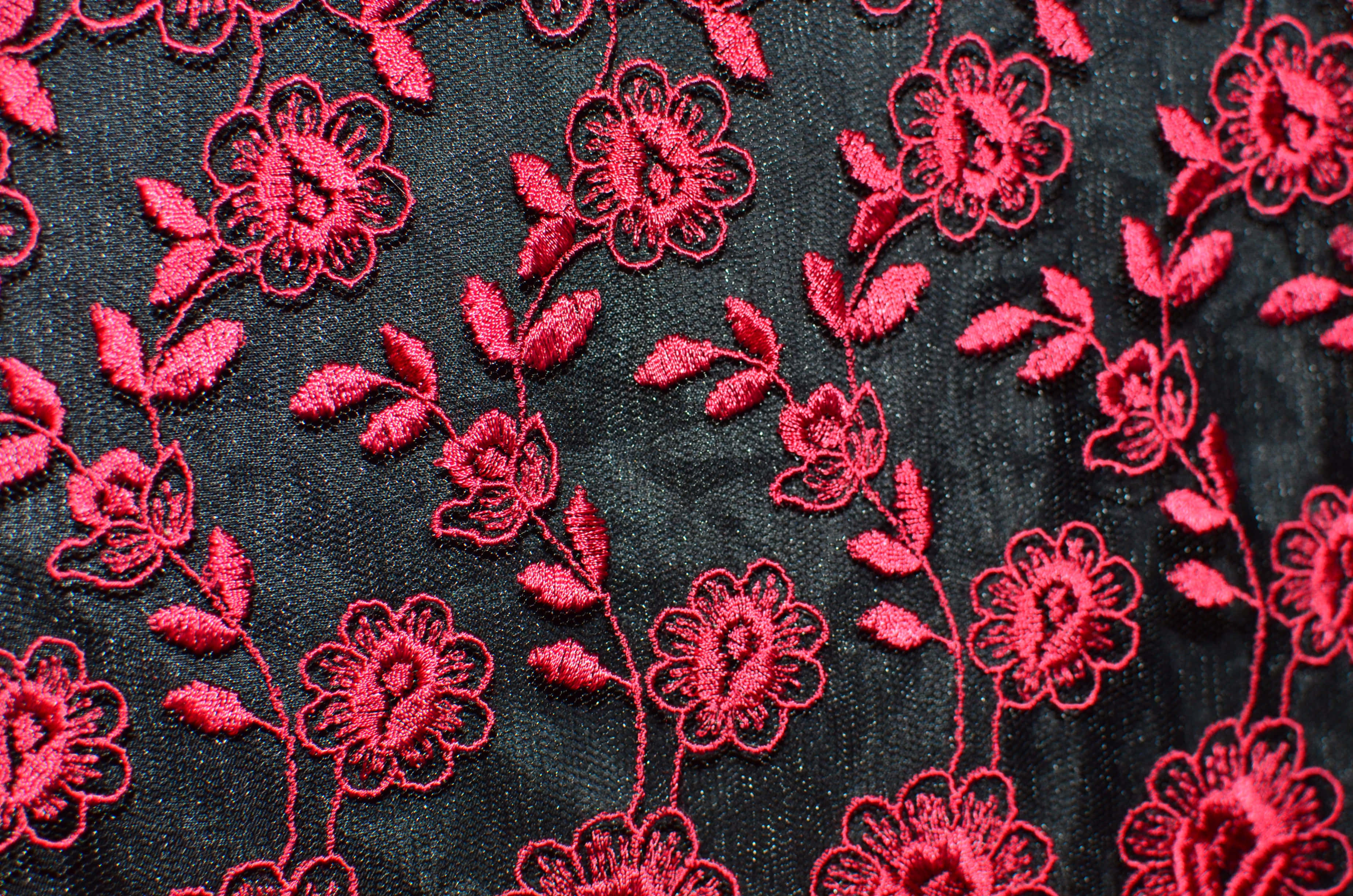 時尚 桌布 壁紙 — 深色紋理布料上精緻紅色花卉刺繡的特寫，展現細緻的針腳和柔和的陰影。
