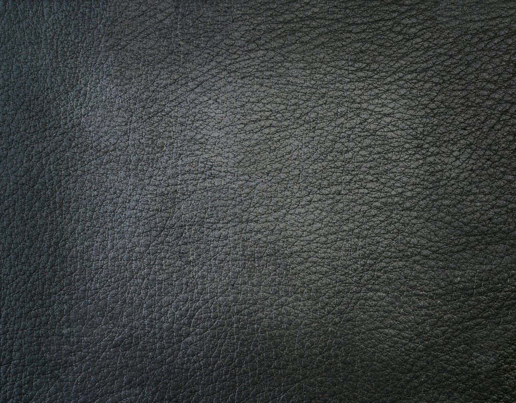 Leather 桌布 壁紙 — 深色紋理皮革表面的特寫，帶有細微的粒面圖案和柔和的光線。