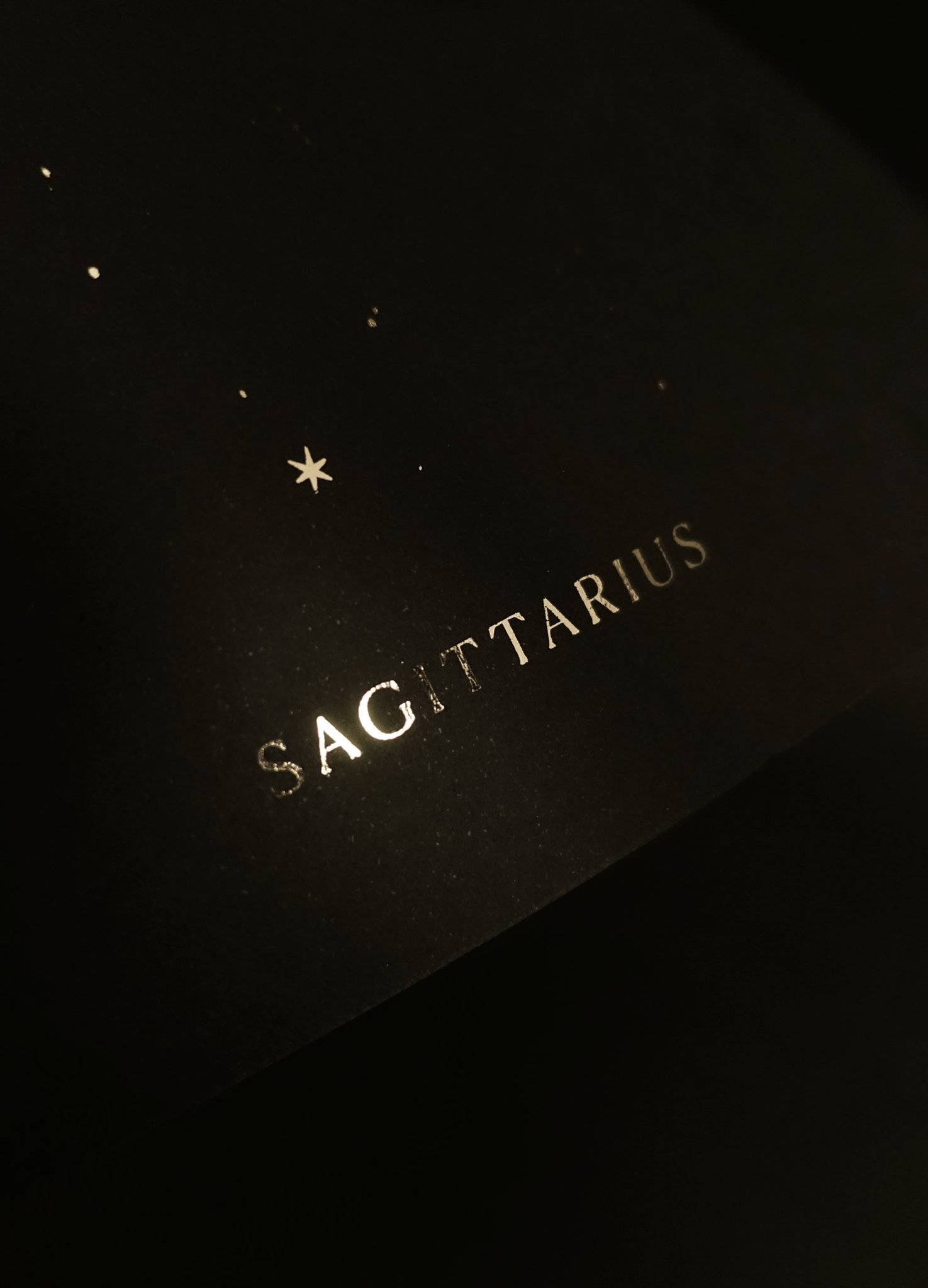 sagittarius 桌布 壁紙 — 深色紋理表面上，以金箔呈現「人馬座」字樣，並有一顆小星星和散落的點狀星星。