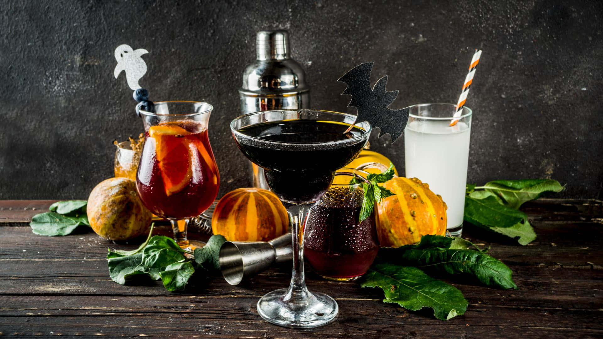 Spooky Cocktails 桌布 壁紙 — 深色鄉村風格桌上展示著恐怖萬聖節雞尾酒，裝飾有南瓜、鬼魂和蝙蝠，背景帶有紋理。