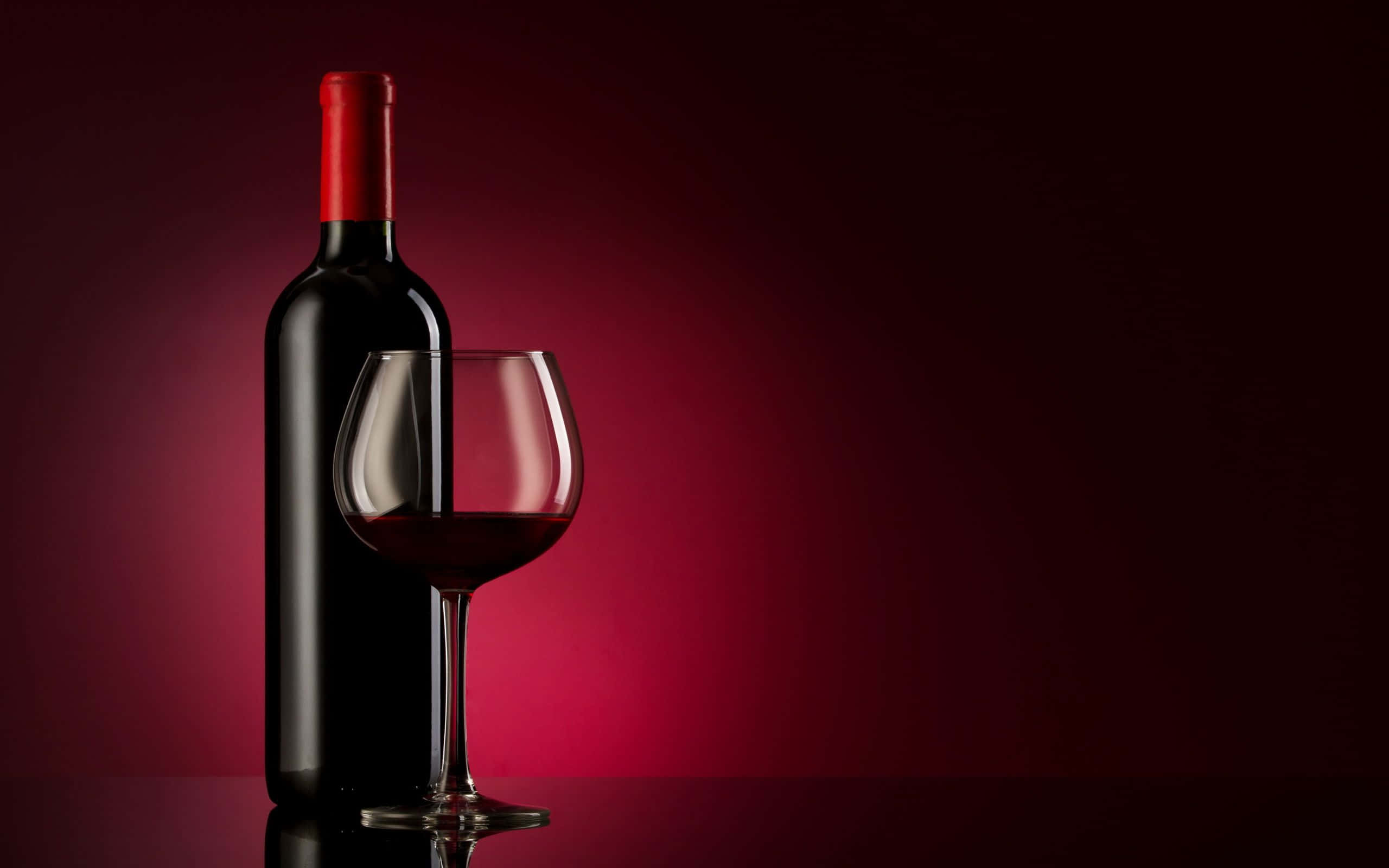 Red Wine Glass 桌布 壁紙 — 深色酒瓶和裝滿紅酒的酒杯，在豐富的漸變紅色背景和柔和燈光下優雅地佇立。