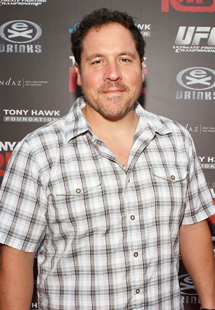 Jon Favreau 桌布 壁紙 — 深色頭髮和鬍鬚的男子在UFC活動背景下穿著格紋襯衫。