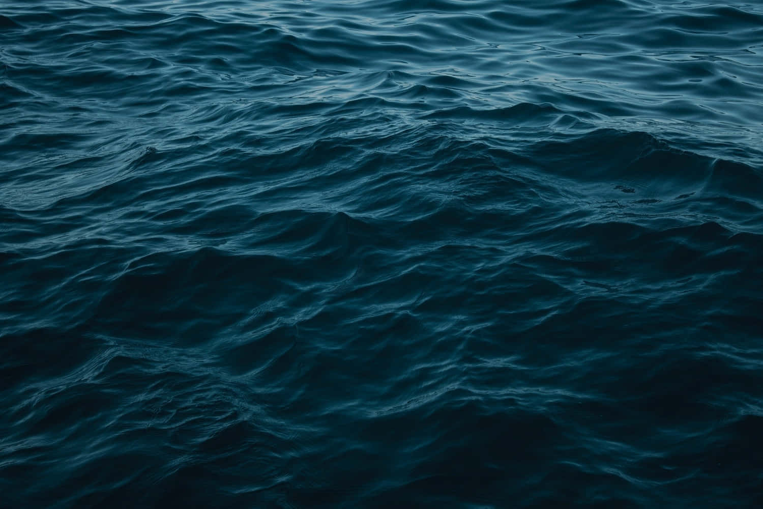 Ocean Water 桌布 壁紙 — 深藍綠色海浪在昏暗燈光下帶有細微紋理漣漪，營造出陰鬱的水面。