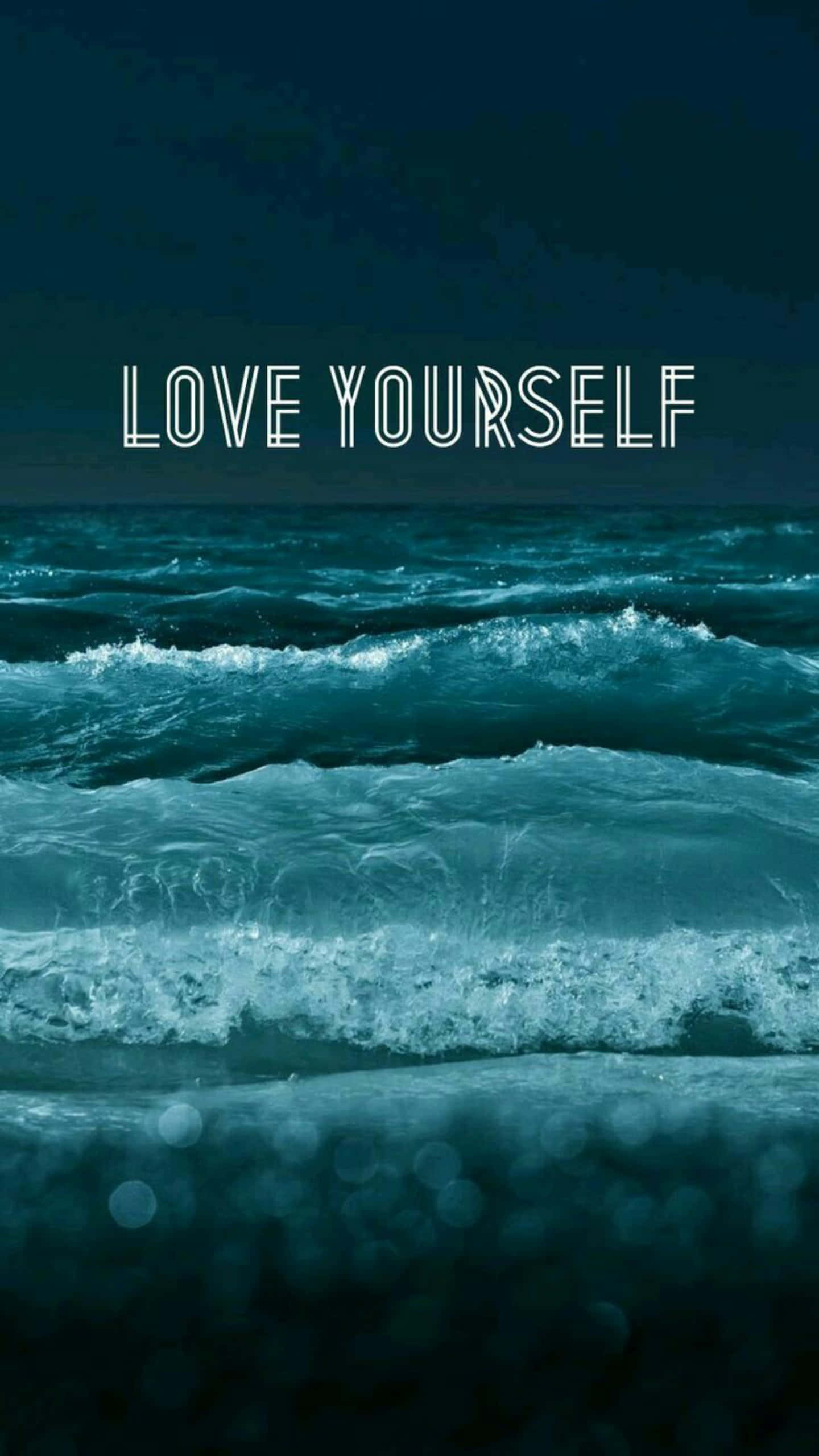 love yourself 桌布 壁紙 — 深藍綠色海浪撞擊出白色泡沫，陰沉天空下閃耀著「愛自己」的文字。