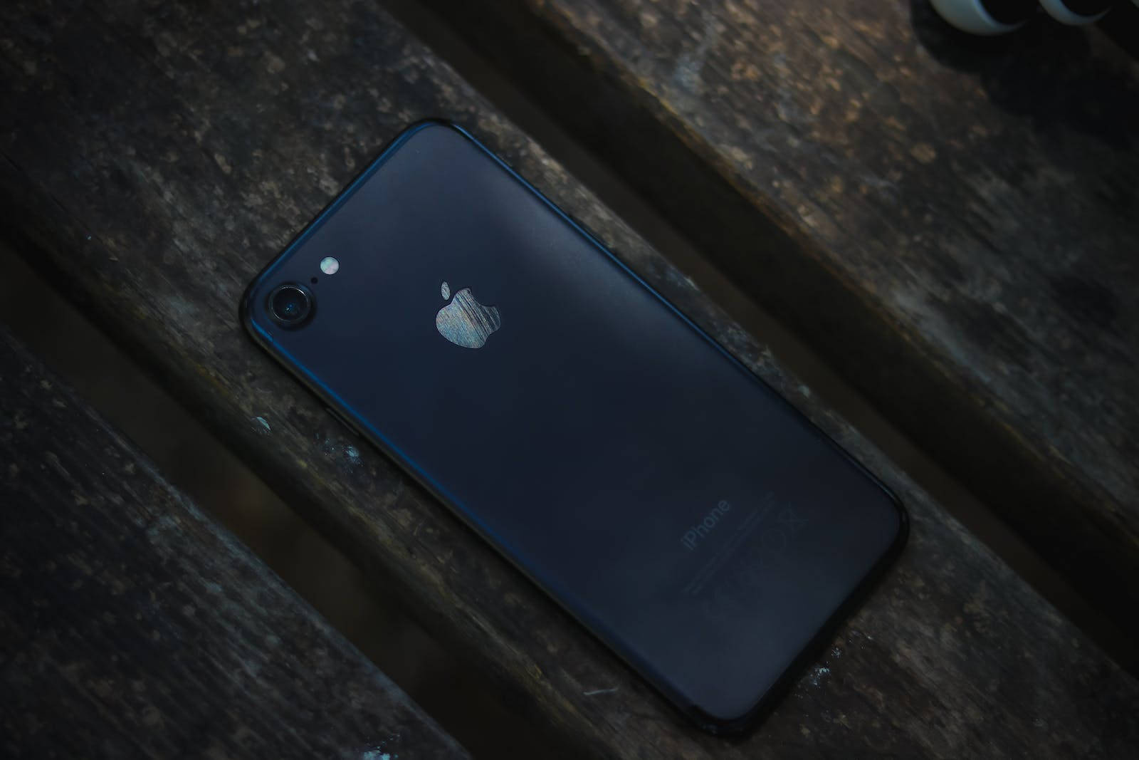 深色 iPhone 桌布 壁紙 — 深藍色iPhone 7在昏暗燈光下擱在風化的木板上。