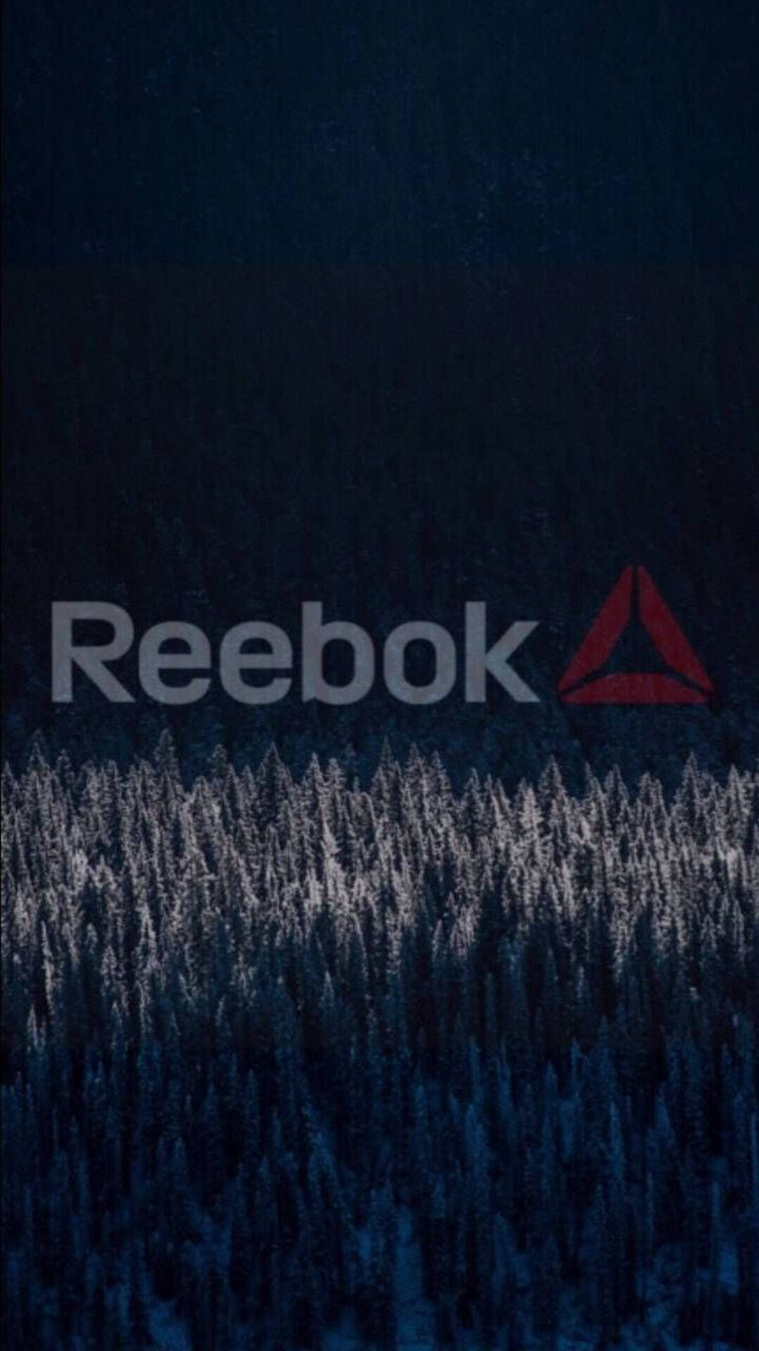 Reebok 桌布 壁紙 — 深藍色冬季森林，樹木覆蓋著雪，發光的 Reebok 標誌漂浮在上方。