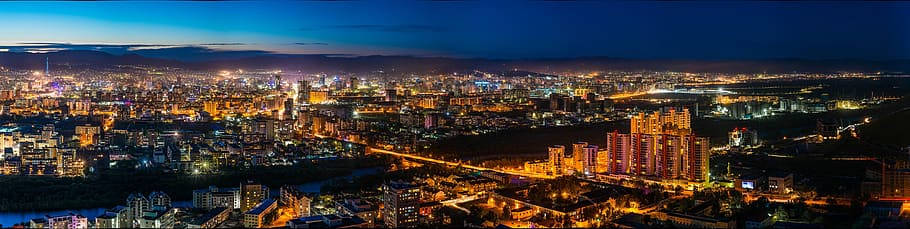 城市 桌布 壁紙 — 深藍色天空下，一座廣闊城市在夜晚的全景視圖，建築物和街道散發著閃爍的燈光。