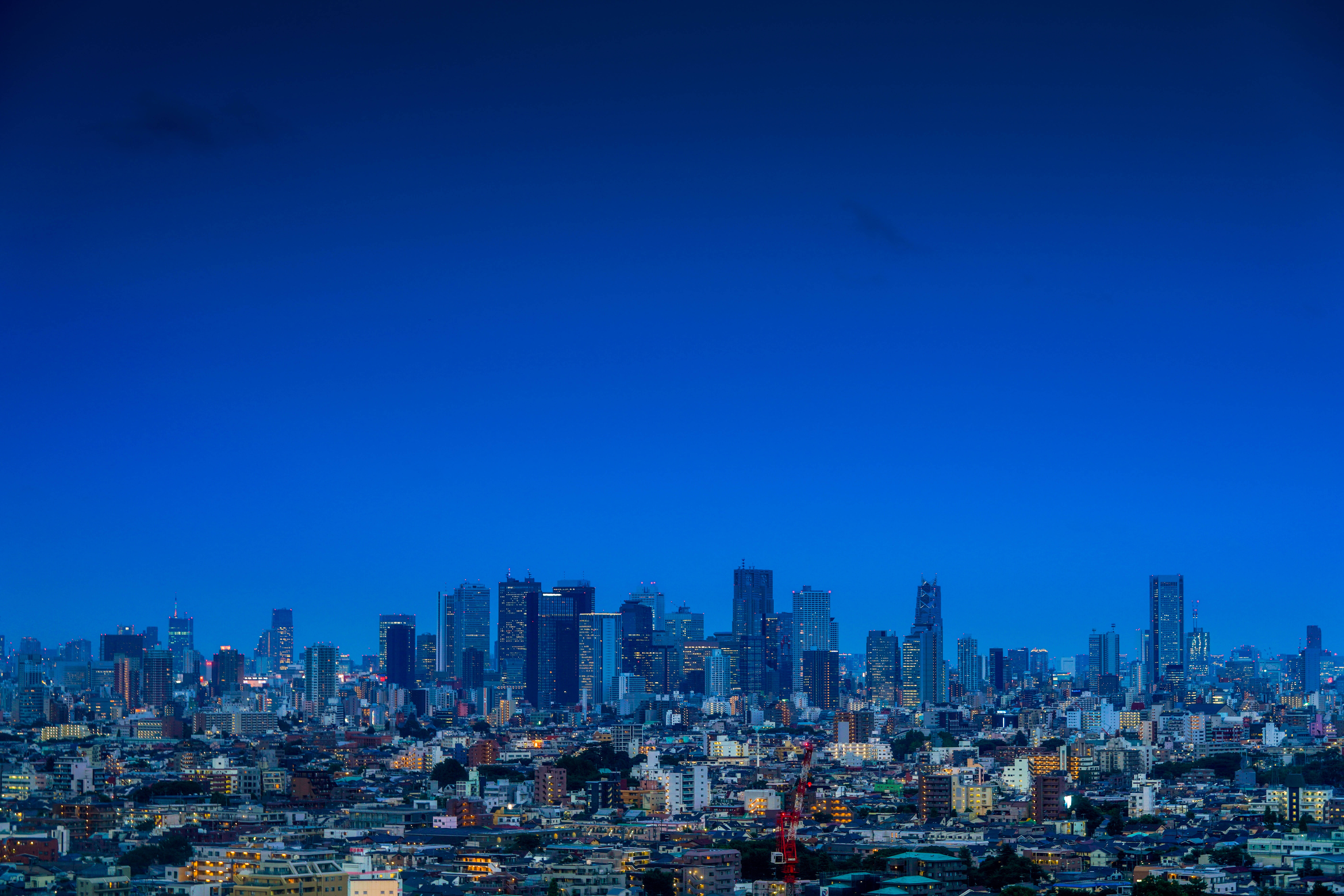 東京 桌布 壁紙 — 深藍色天空下，廣闊的城市景觀在黃昏時分，閃爍的摩天大樓和住宅建築。