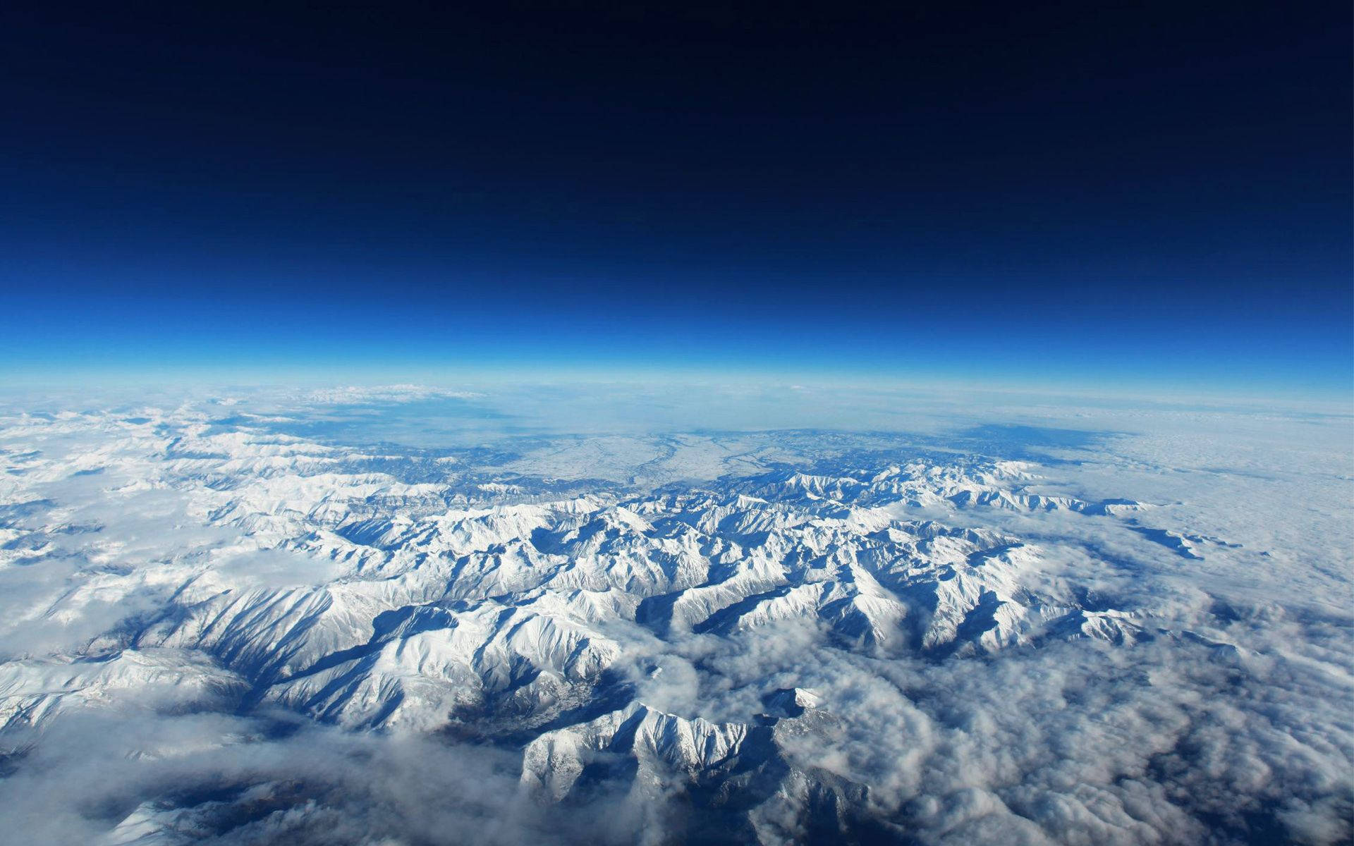 白雪皚皚的山峰在晴朗的藍天下聳立於雲層之上。 — 4K 地球 壁紙