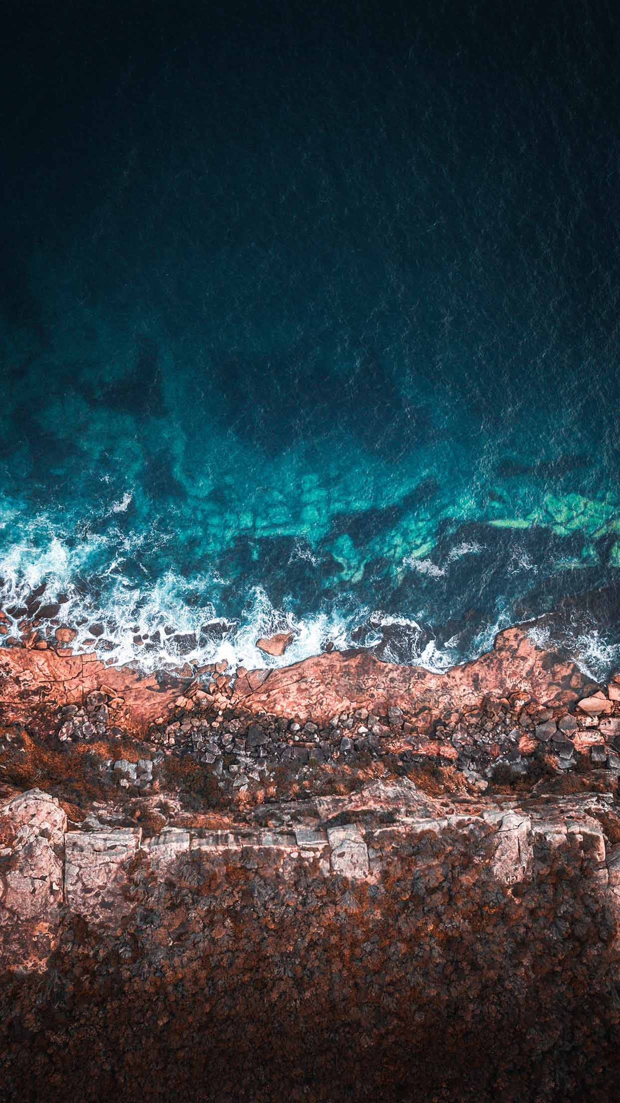 waves 桌布 壁紙 — 深藍色天空下，碧綠色的海浪拍打著崎嶇的紅褐色海岸懸崖的航拍視圖。
