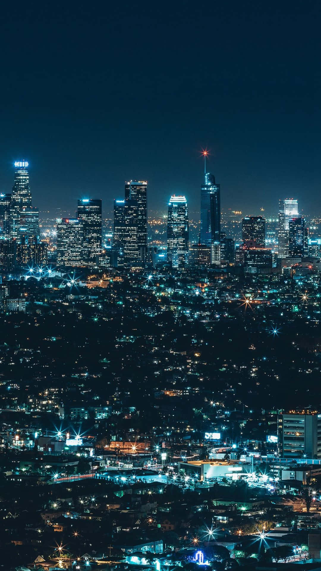 City Night 桌布 壁紙 — 深藍色天空下，閃爍的摩天大樓和街燈構成的廣闊城市景觀的夜間空拍圖。
